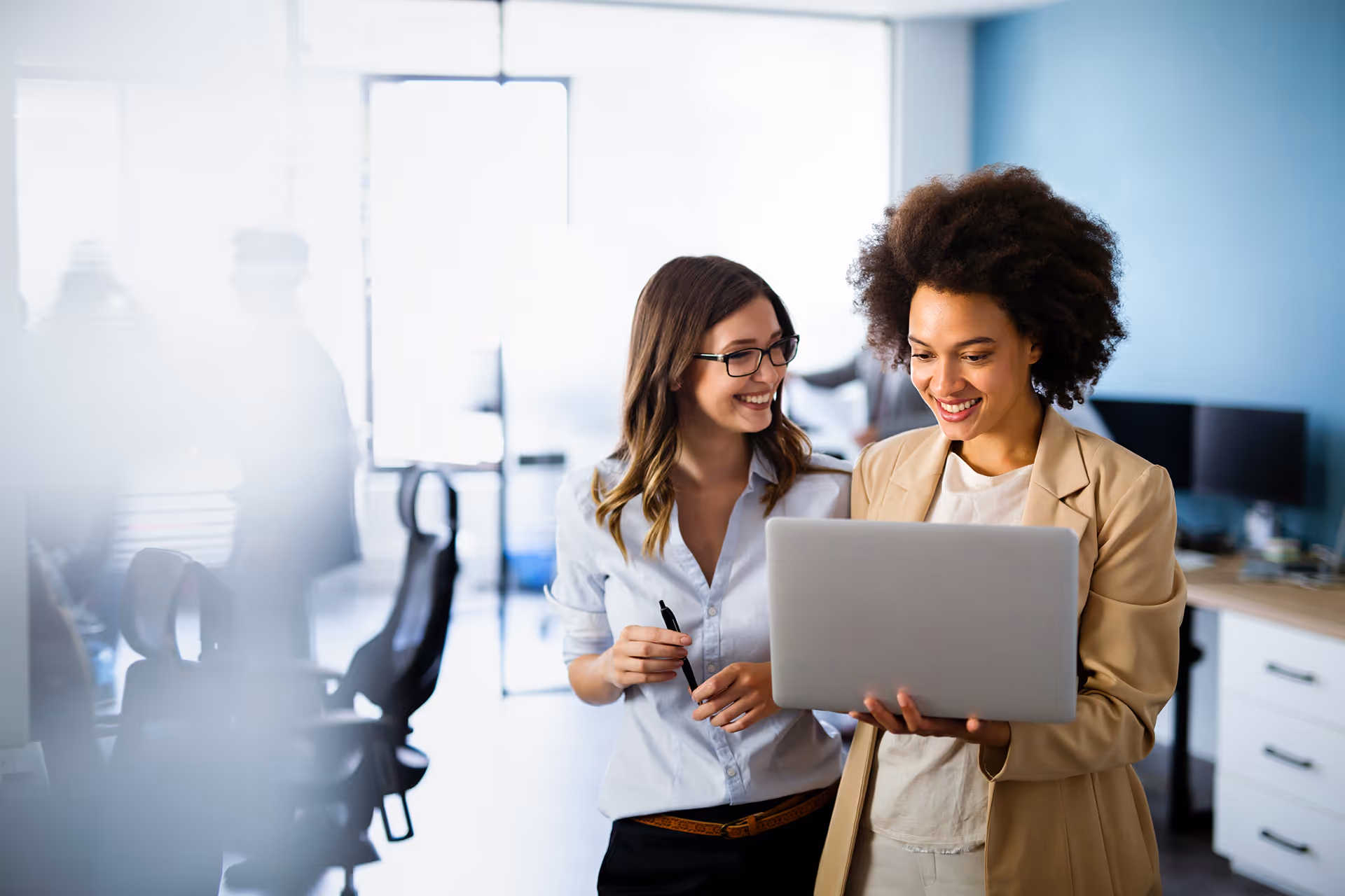 A woman holding a laptop showing her friend something