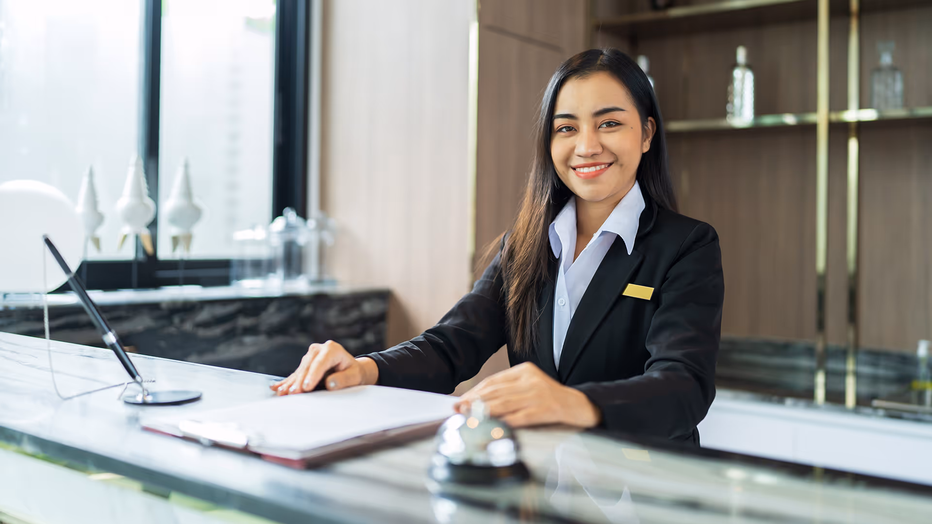 Smiling receptionist waiting at a hotel check-in desk — representing accommodation provider merchant accounts