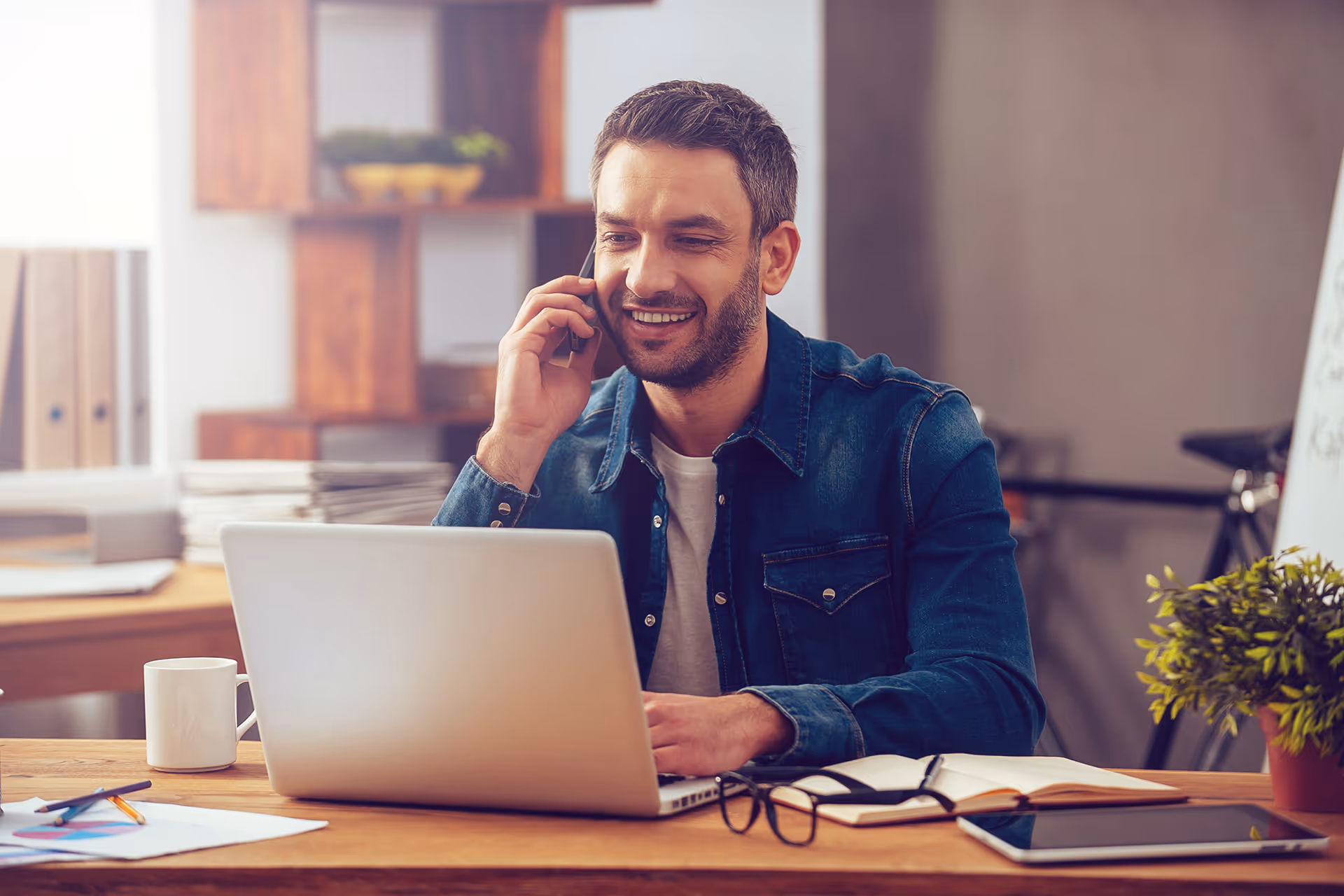A man sat in front of a laptop using a phone