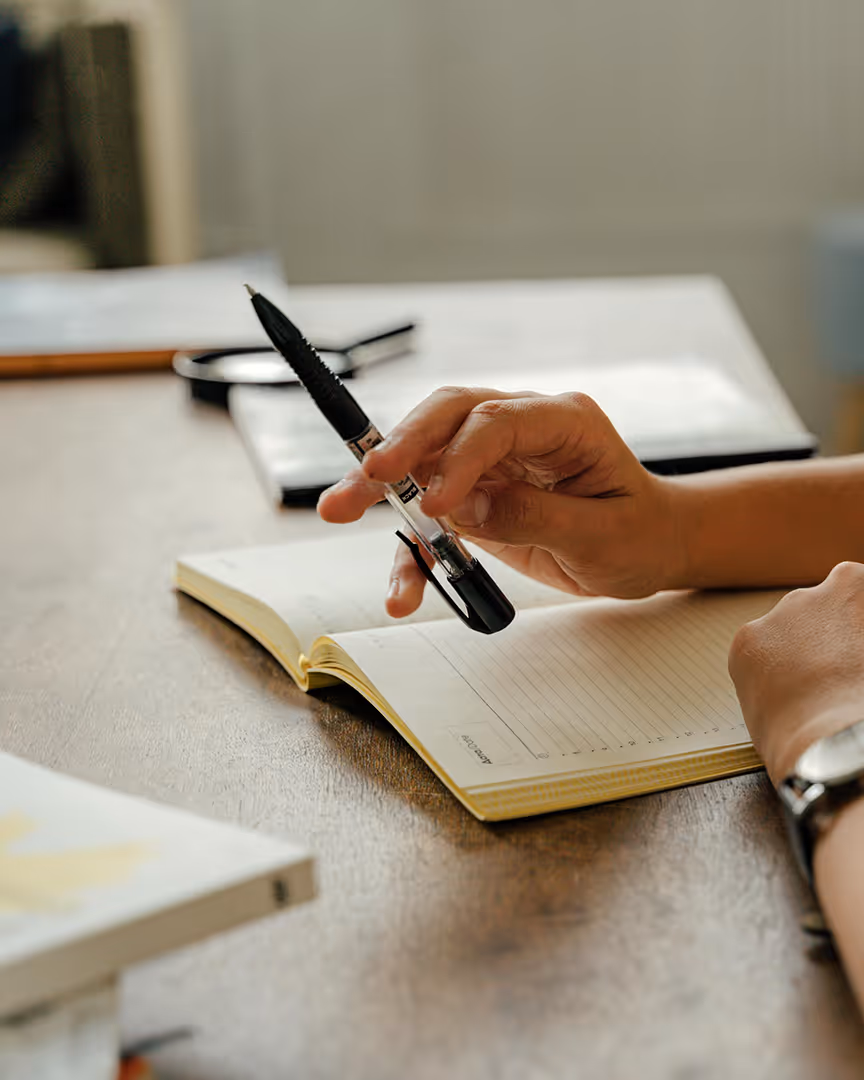 Holding a pen over a notebook, representing questions to ask about travel payment solutions