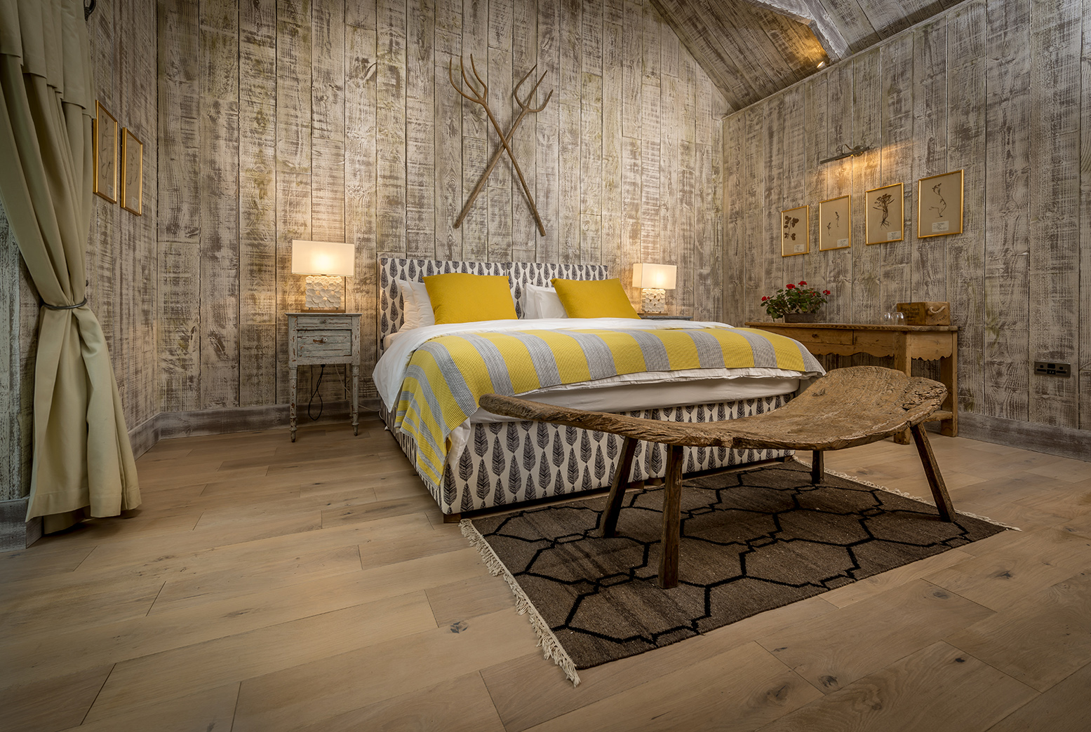 Rustic spa retreat like bedroom interior with dark wood walls, a wooden dresser, a cozy armchair with a cushion, a small wooden chair, and a bed partially covered with a fur throw.