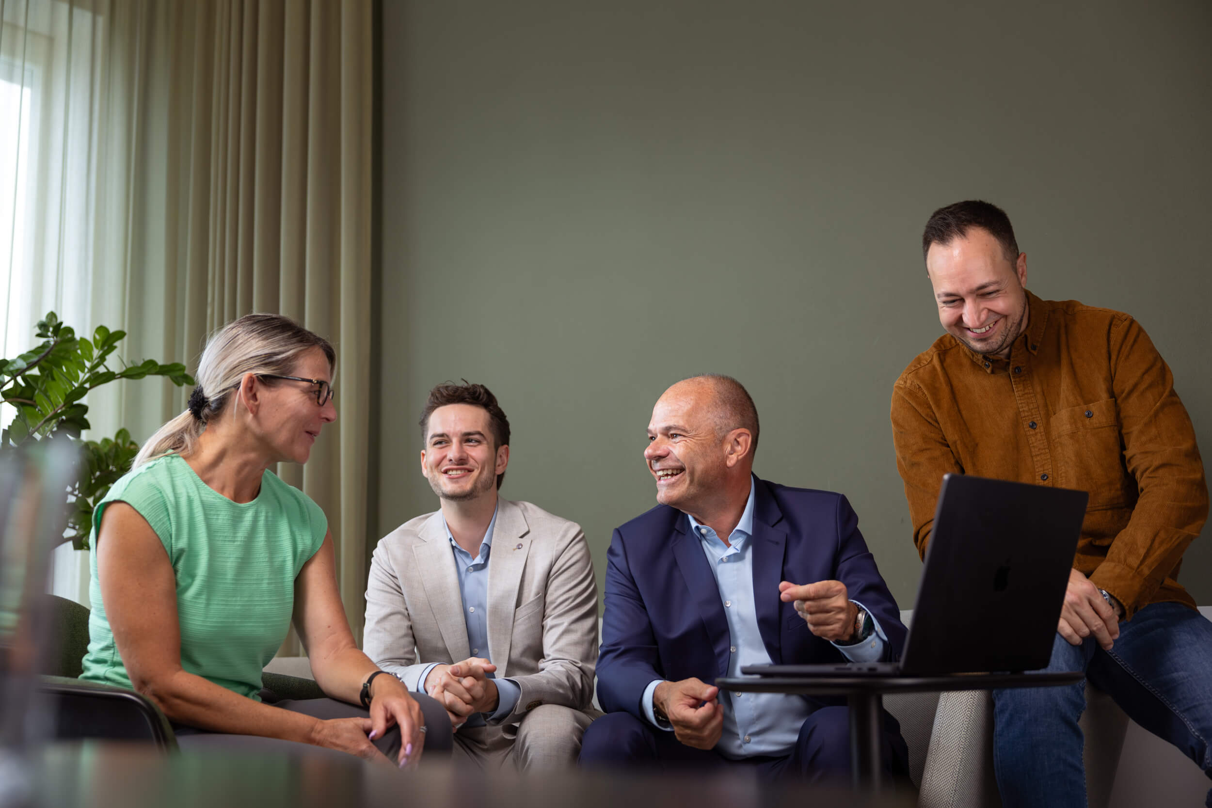 Vier Personen in einem Gespräch in einem Büro, drei sitzen und eine lehnt sich an einen Tisch mit einem Laptop.