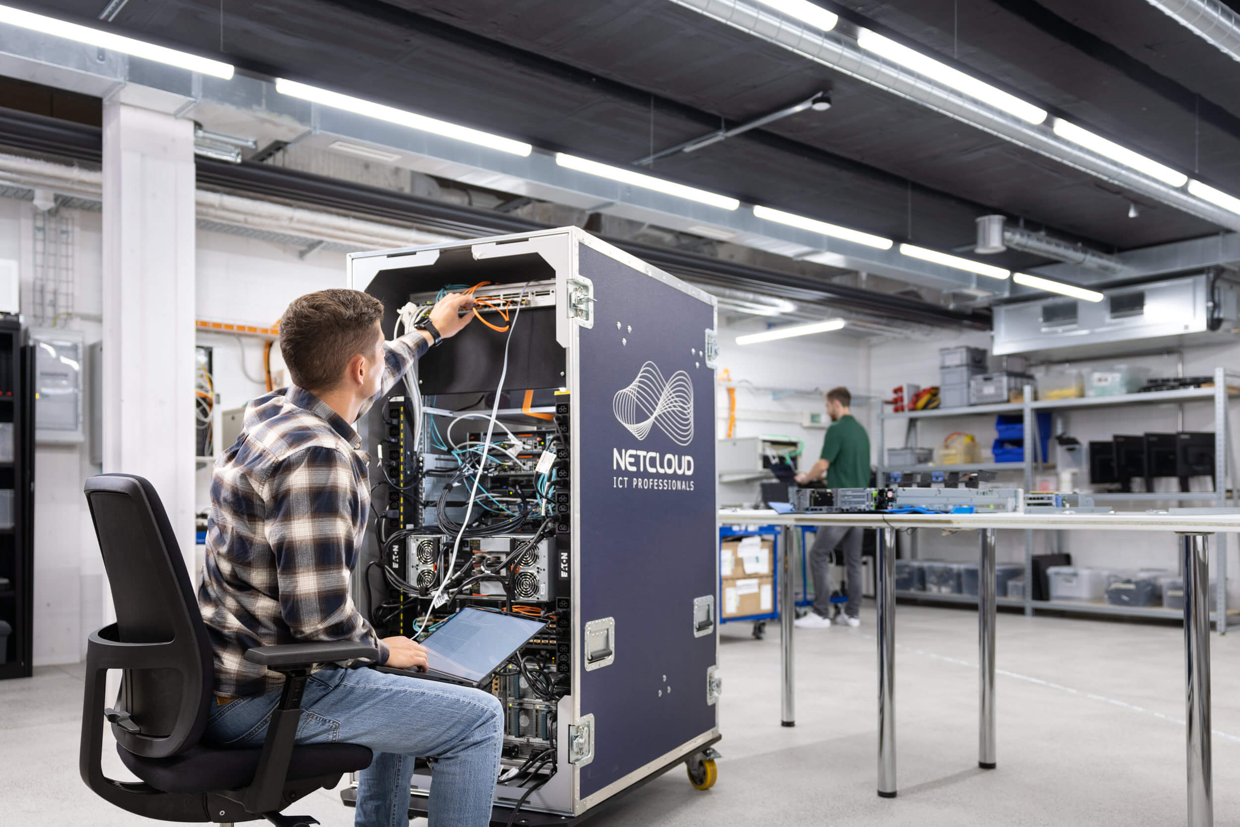 Techniker in einem Büro mit Server-Racks, der an einem Serverkabel arbeitet und einen Laptop benutzt.