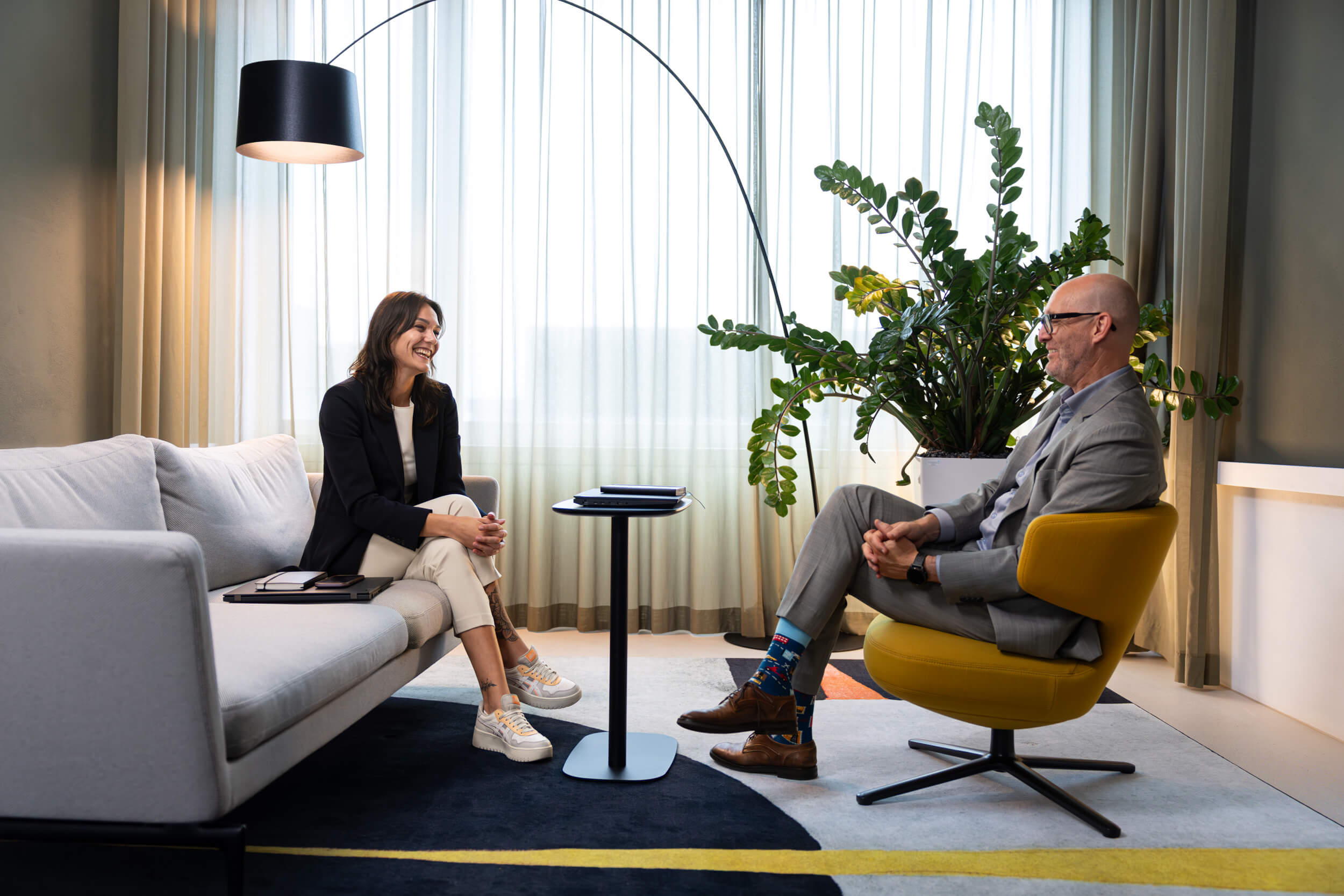 Eine Frau und ein Mann sitzen sich in einem modernen Wohnzimmer gegenüber und führen ein Gespräch.