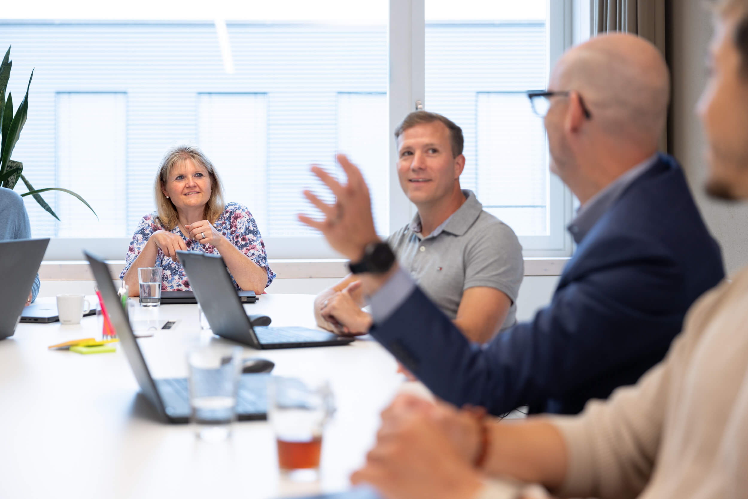 Gruppe von Berufstätigen in einem Meetingraum, die an einem Tisch sitzen und sich angeregt unterhalten.