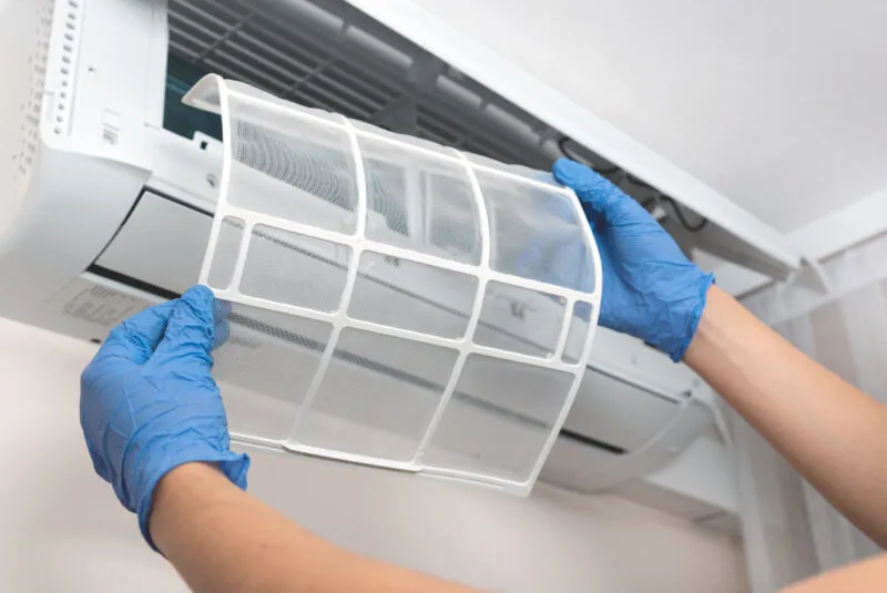 Gloved hands removing air conditioner filter for cleaning or maintenance