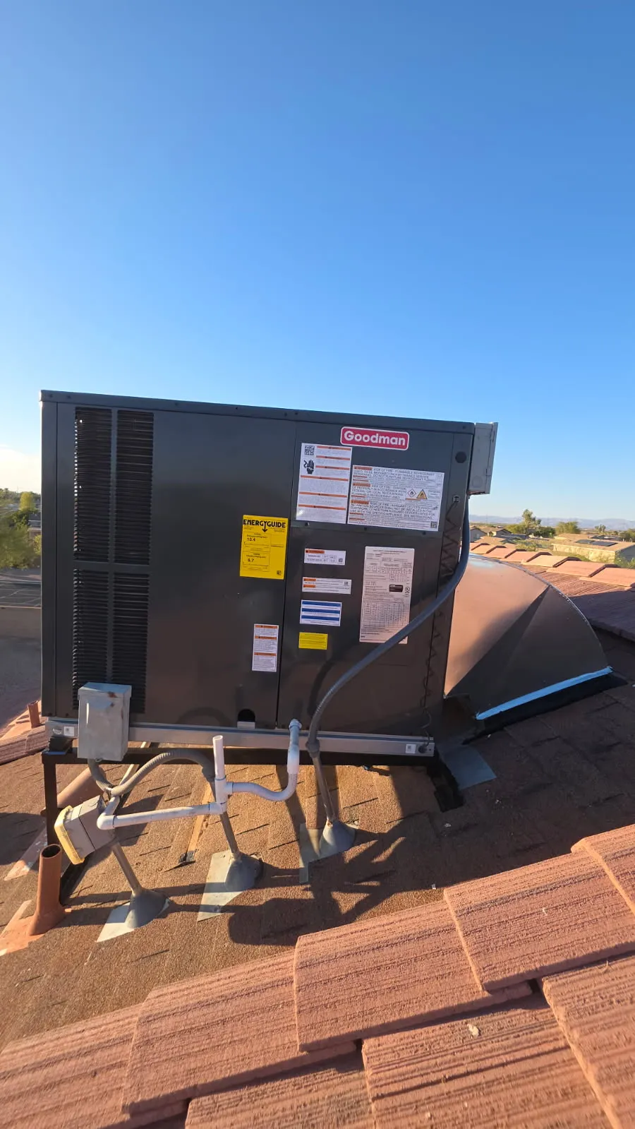 Goodman HVAC unit installed on a tiled roof against blue sky