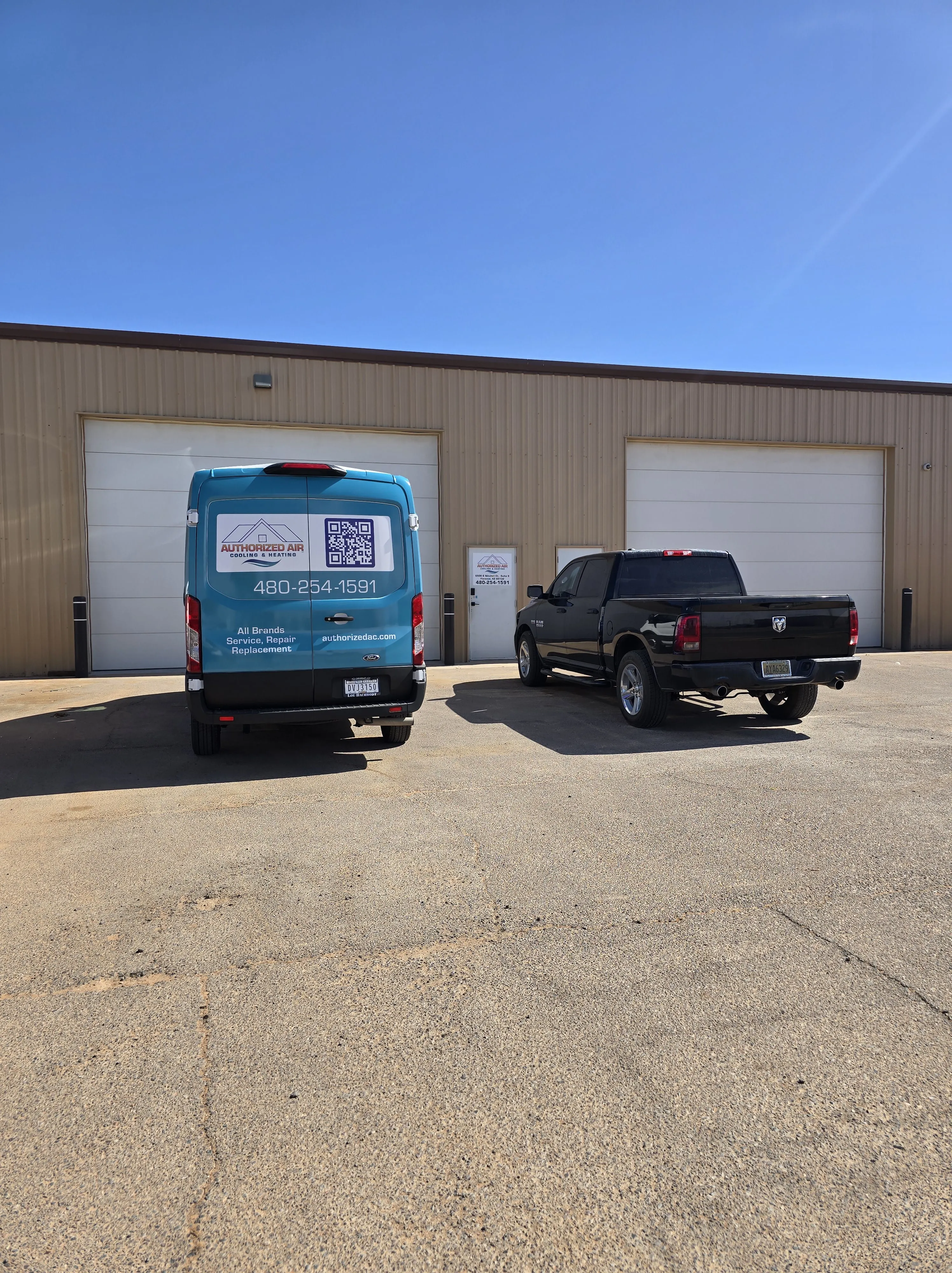 Blue van and black truck parked outside industrial building on sunny day