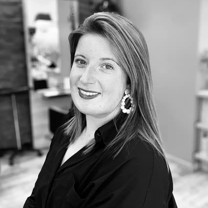 Femme souriante aux cheveux lisses et longs portant une chemise noire et de grandes boucles d'oreilles rondes en perles.