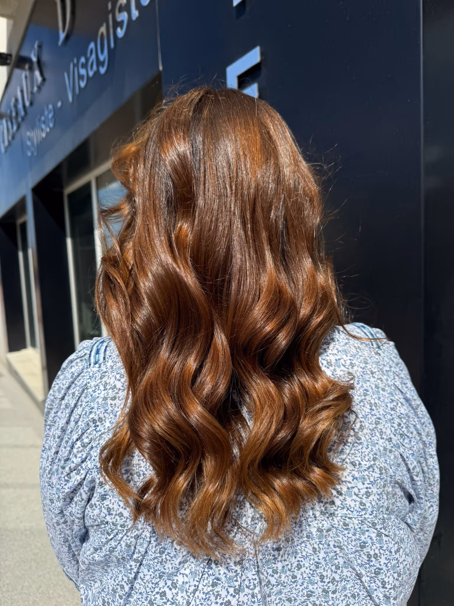 Cheveux longs ondulés couleur auburn brillant sur une personne portant un chemisier à motif floral bleu.