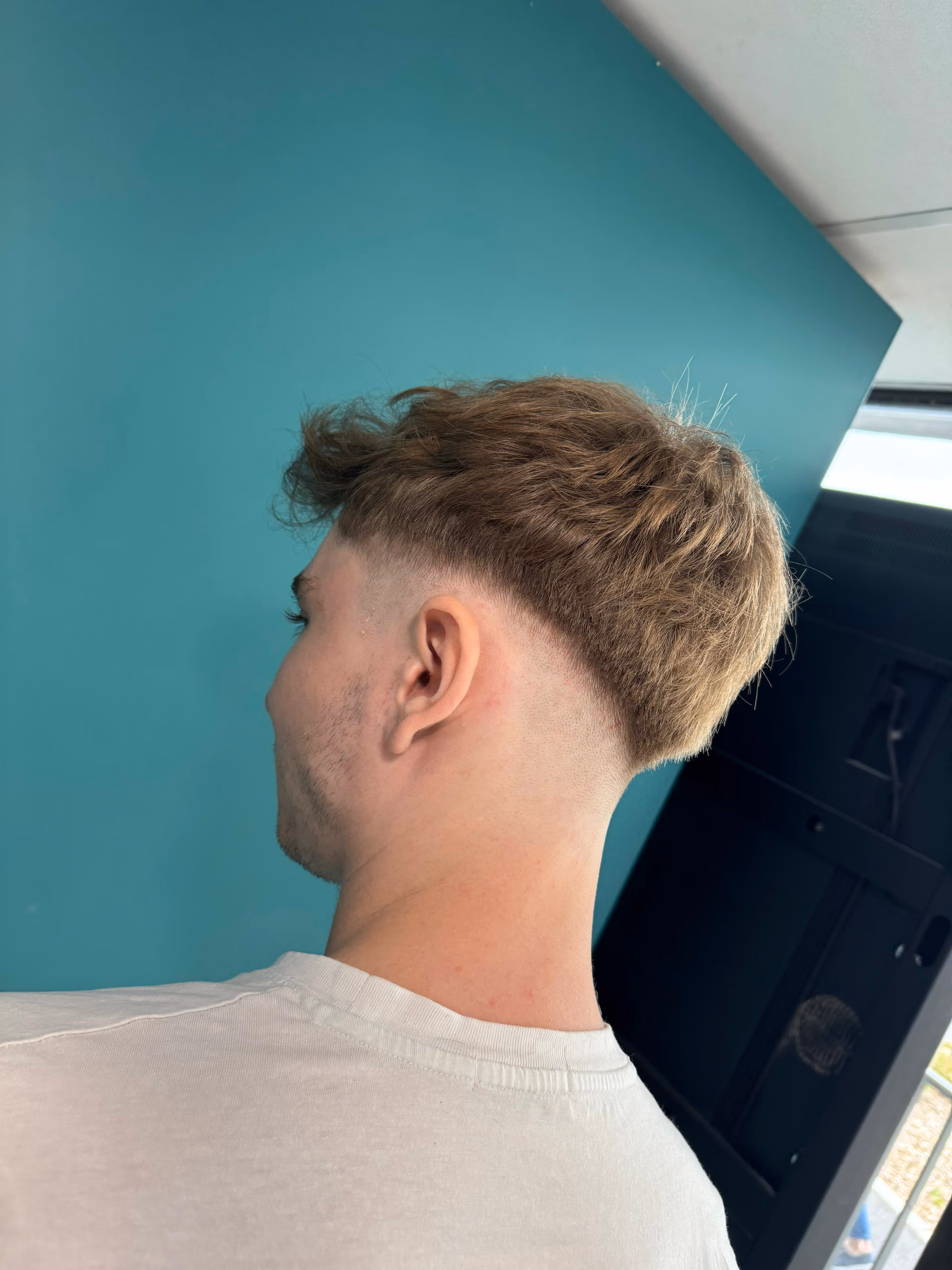 Jeune homme de profil avec une coupe de cheveux dégradée sur les côtés et des cheveux plus longs sur le dessus.