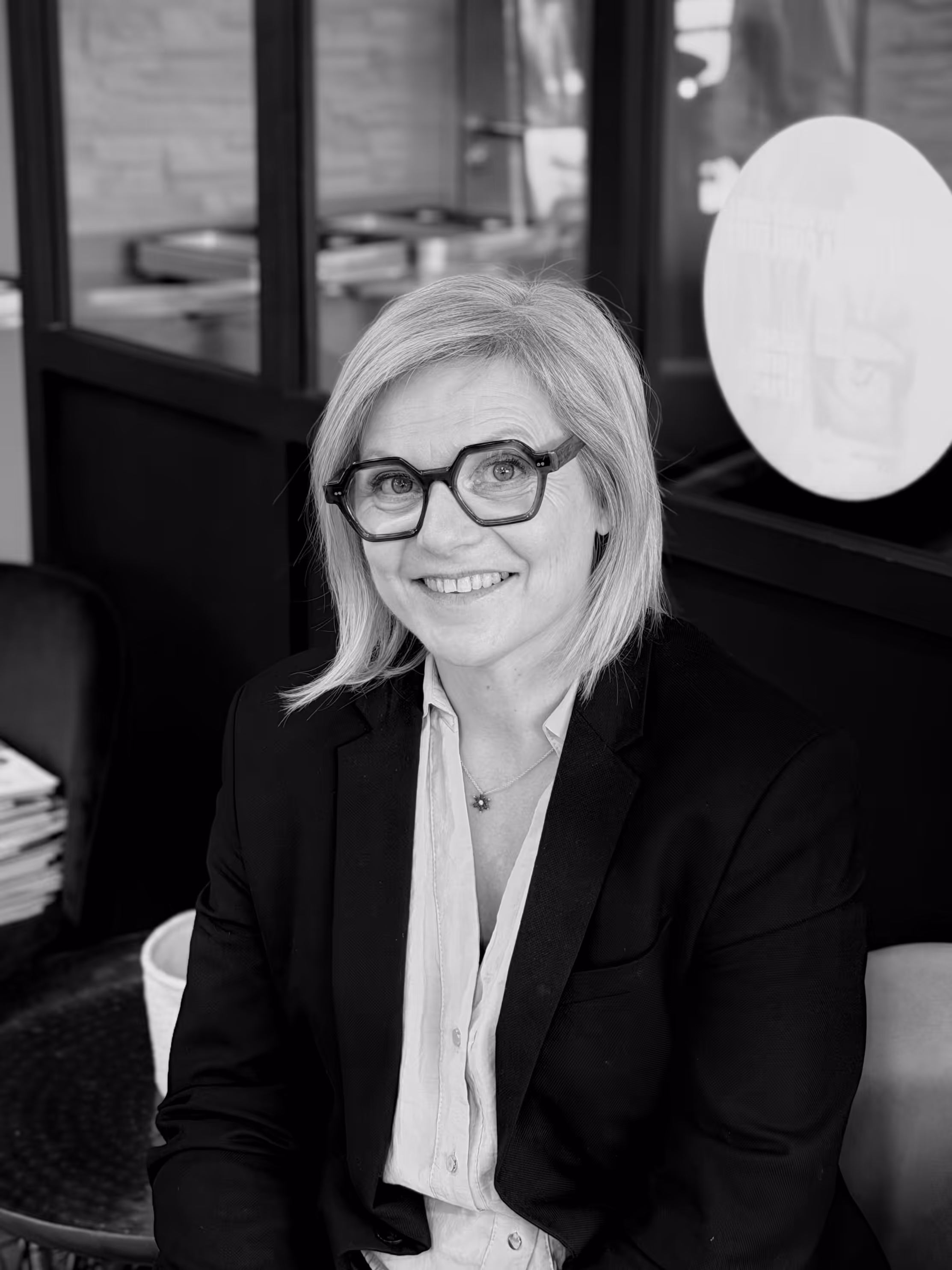 Jeune femme assise à l'intérieur d'un salon, portant un blazer avec un badge nommé Shaina.