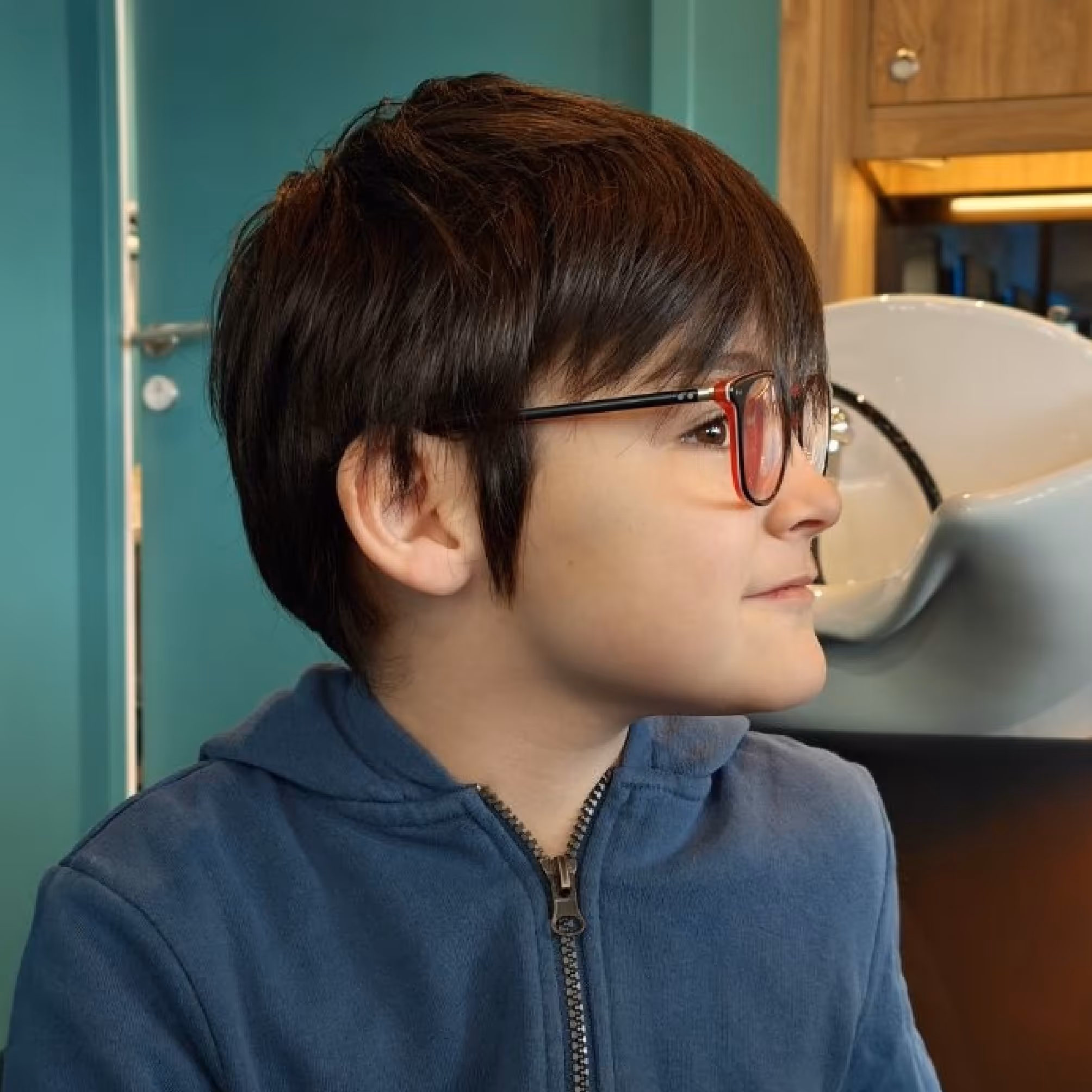 Portrait de profil d’un enfant avec des lunettes noires et rouges portant un sweat à capuche bleu.