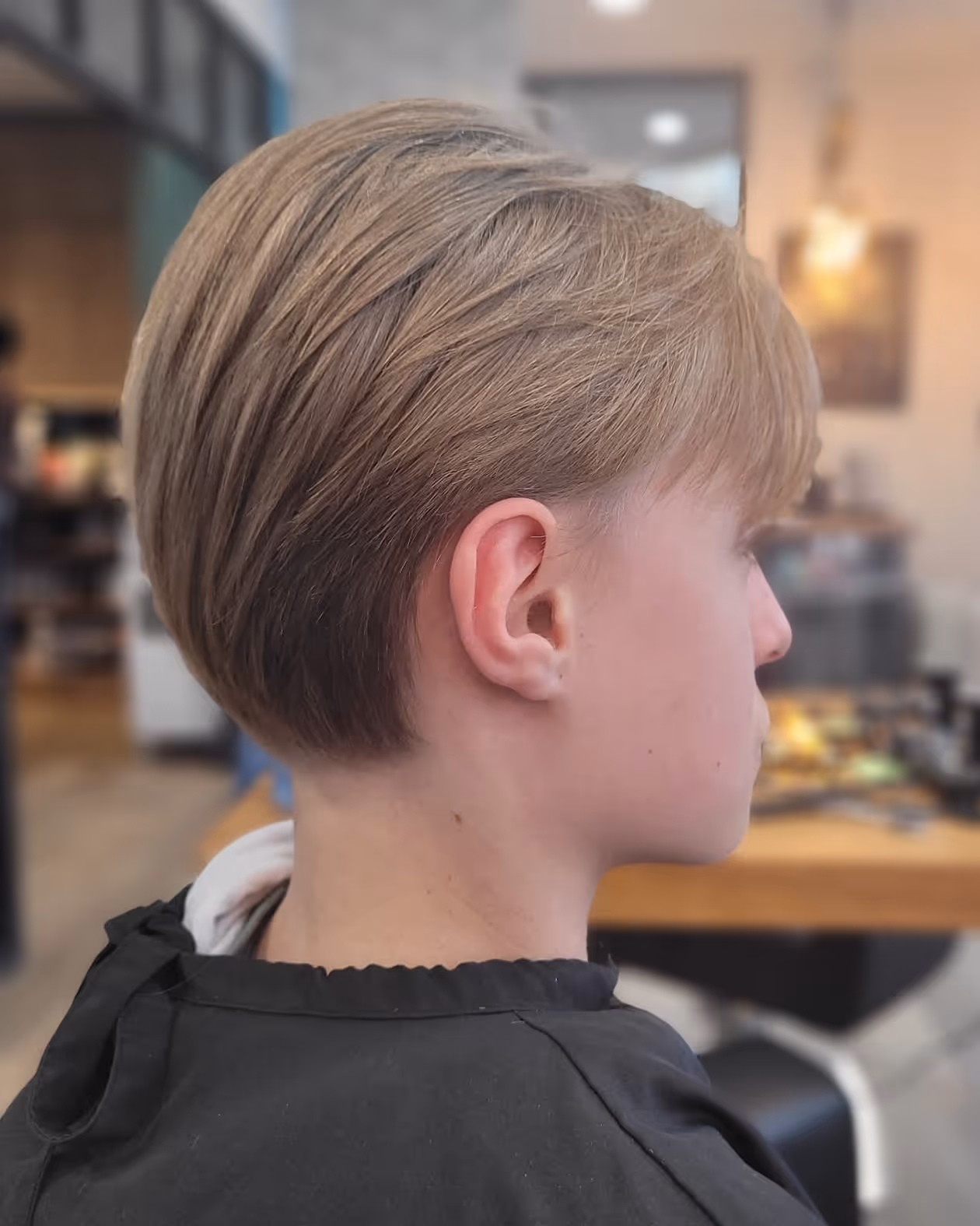 Profil latéral d'une personne avec une coupe de cheveux courte, lisse et bien coiffée, en intérieur flou.