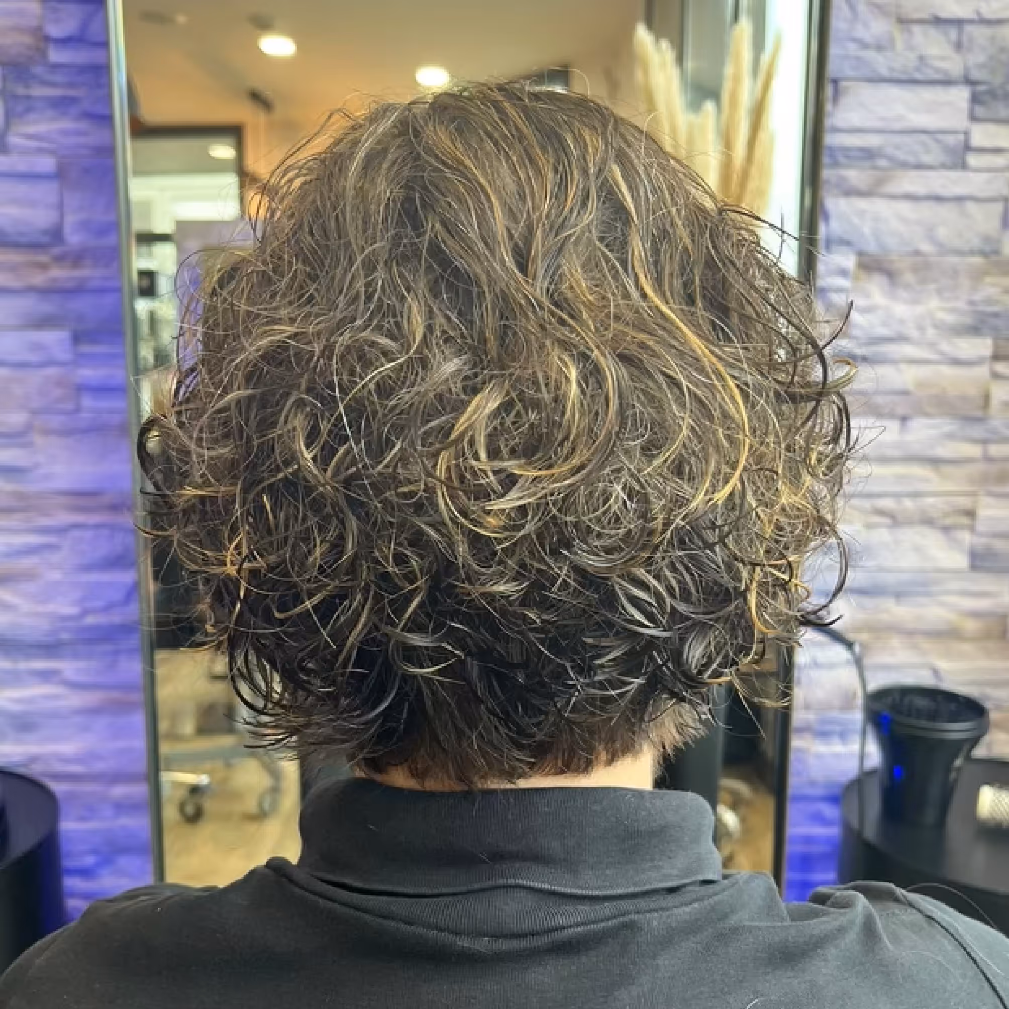 Vue arrière de cheveux courts bouclés avec des reflets blonds dans un salon de coiffure.