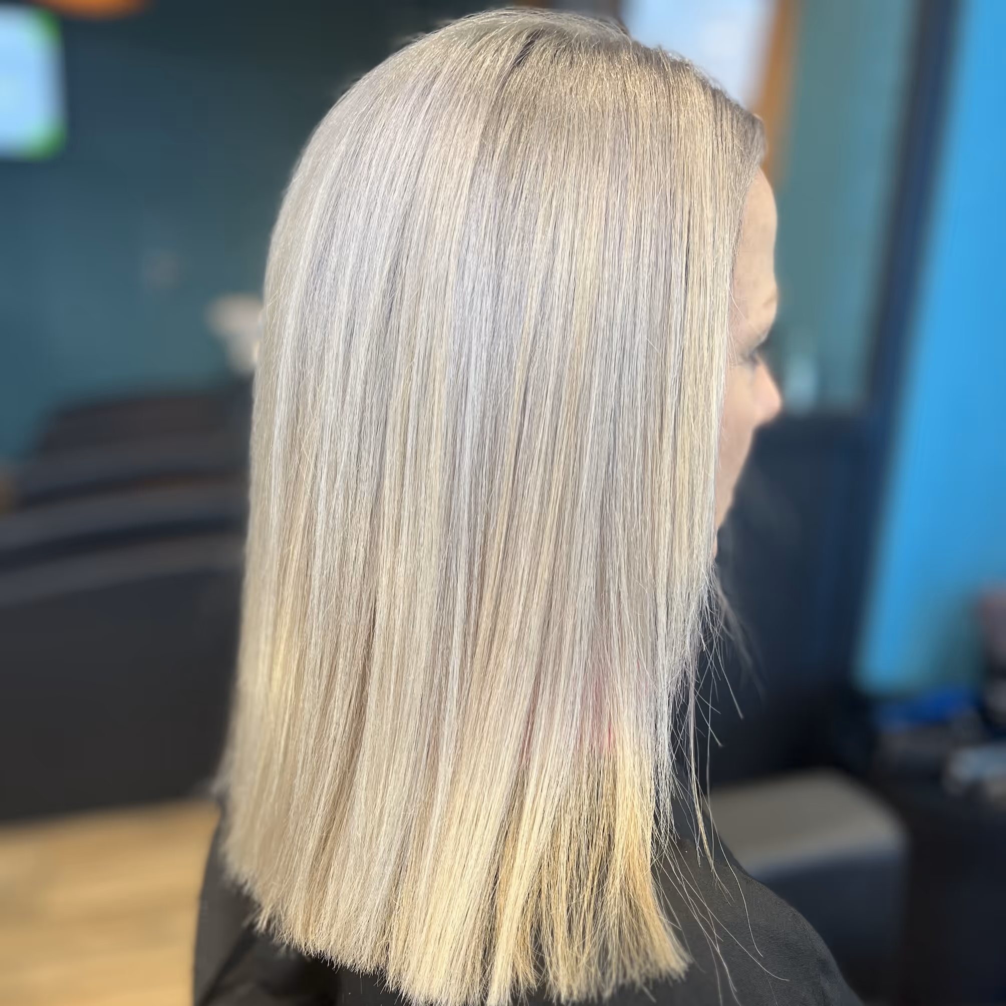 Femme avec cheveux blonds lisses et mi-longs vus de profil dans un salon de coiffure.
