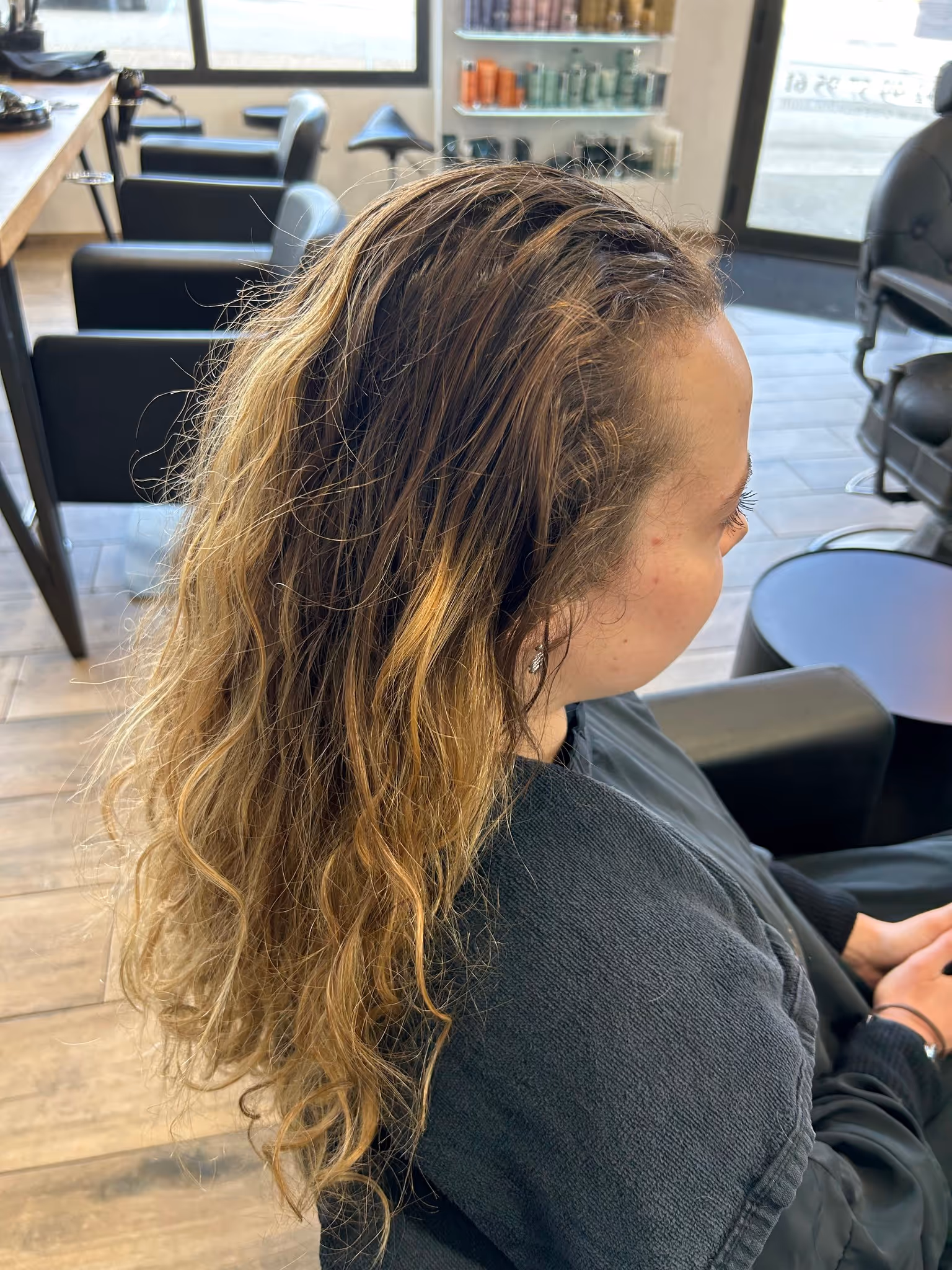 Femme assise dans un salon de coiffure avec de longs cheveux bouclés blond foncé et clair.