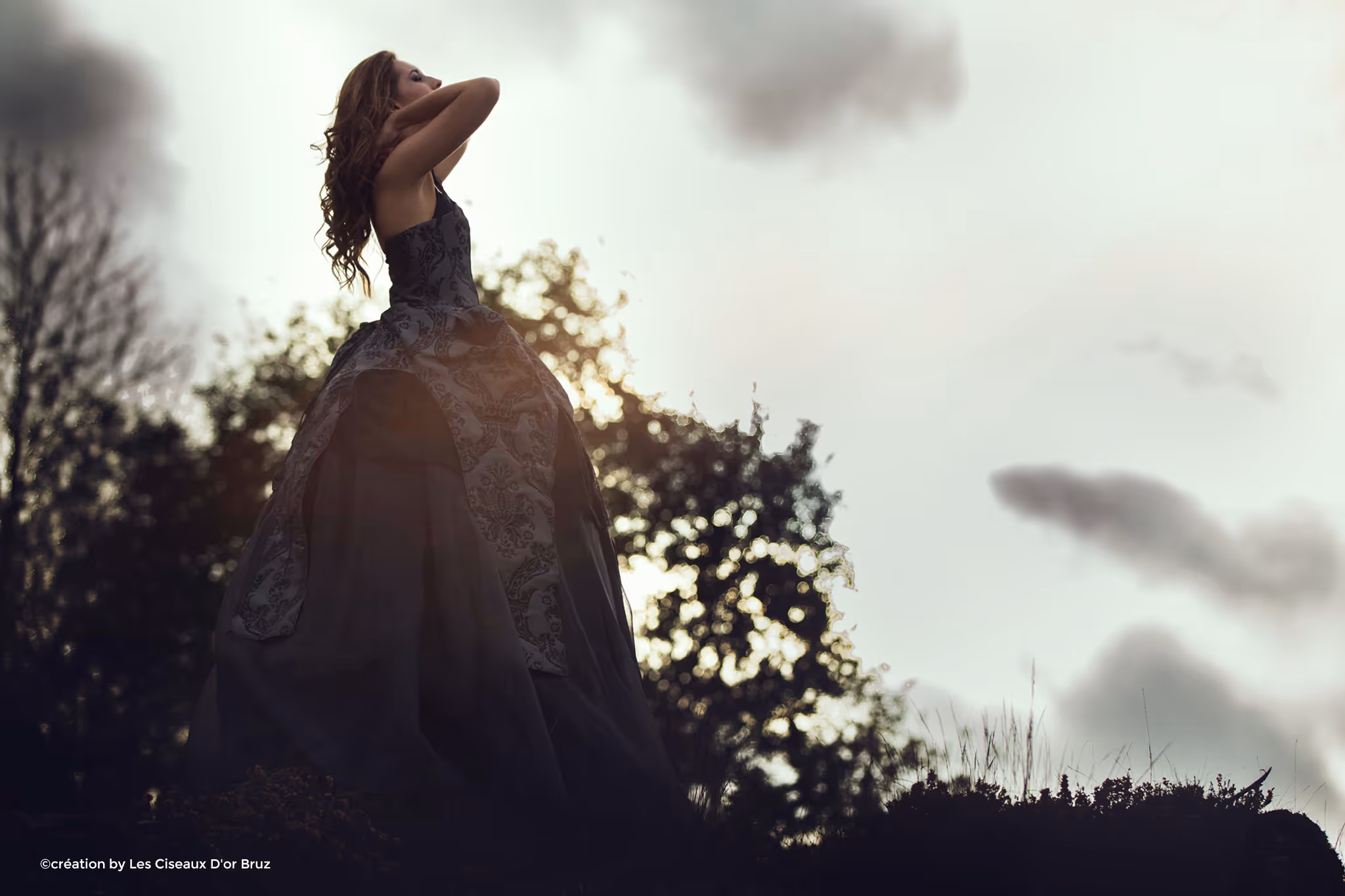 Femme en robe noire élégante avec motifs se tenant dehors au coucher du soleil.