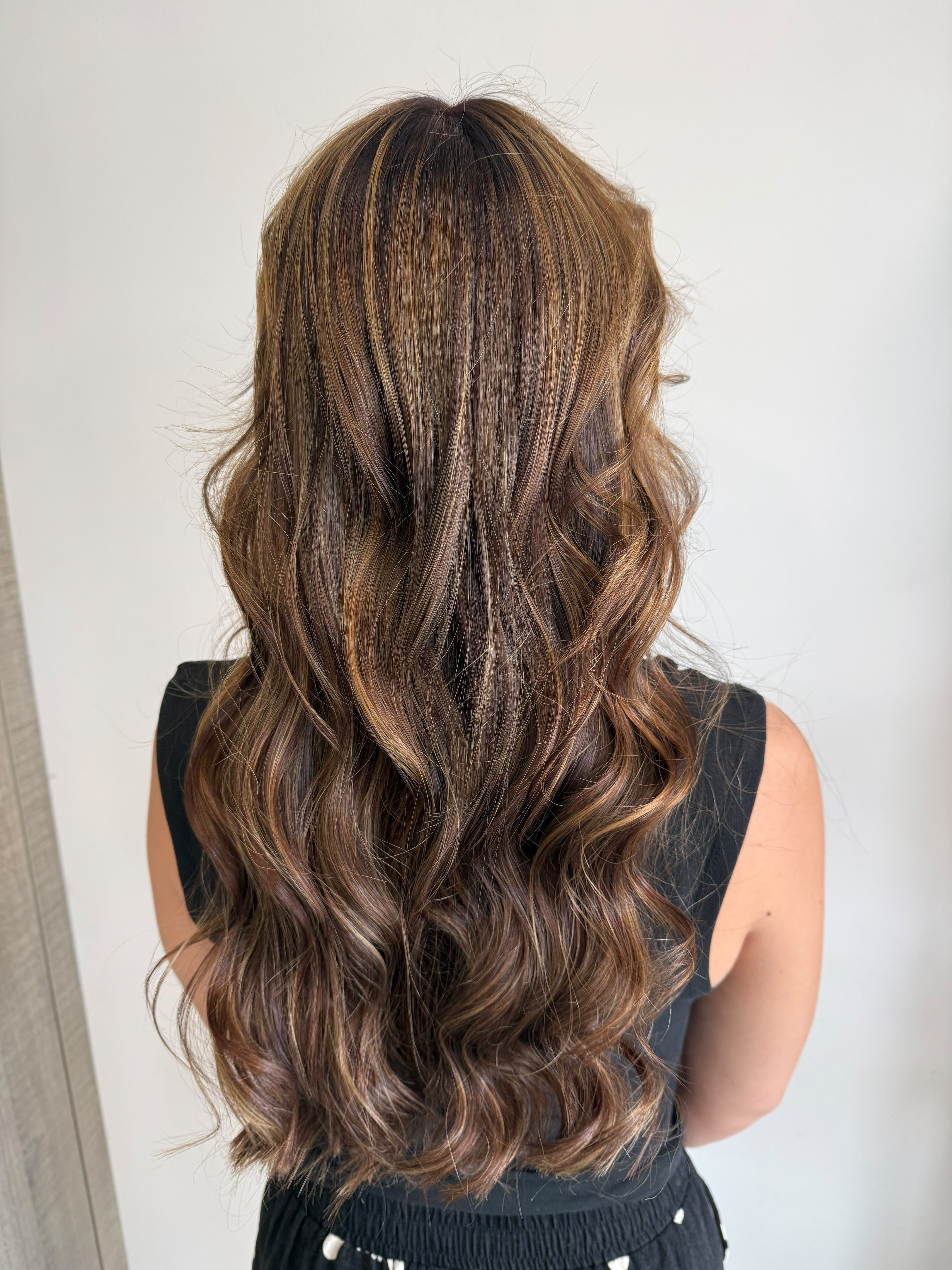 Cheveux longs bouclés avec des mèches blondes vues de dos sur une personne portant un haut rayé blanc et noir.
