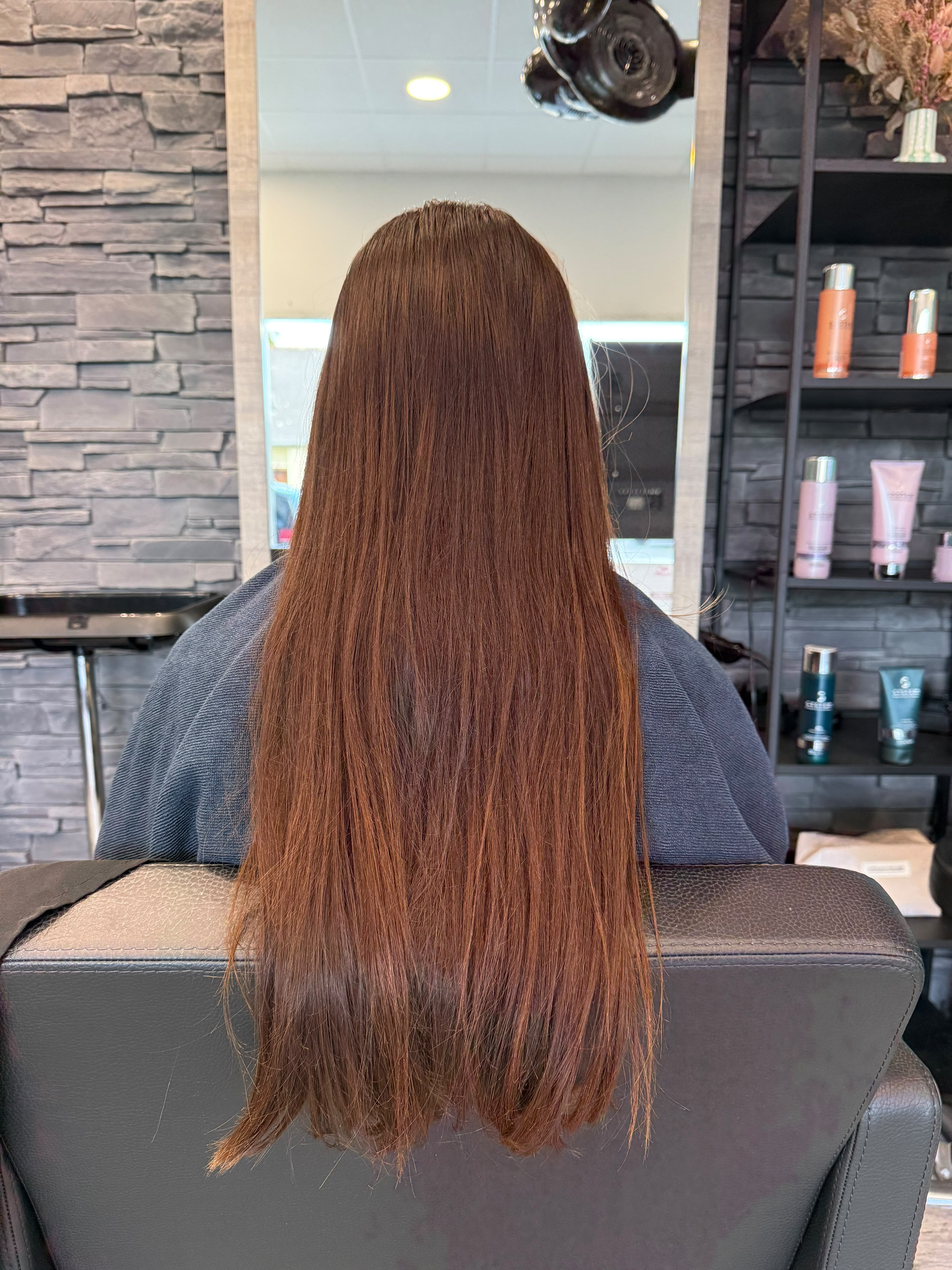 Cheveux longs, épais et ondulés vus de dos dans un salon de coiffure.