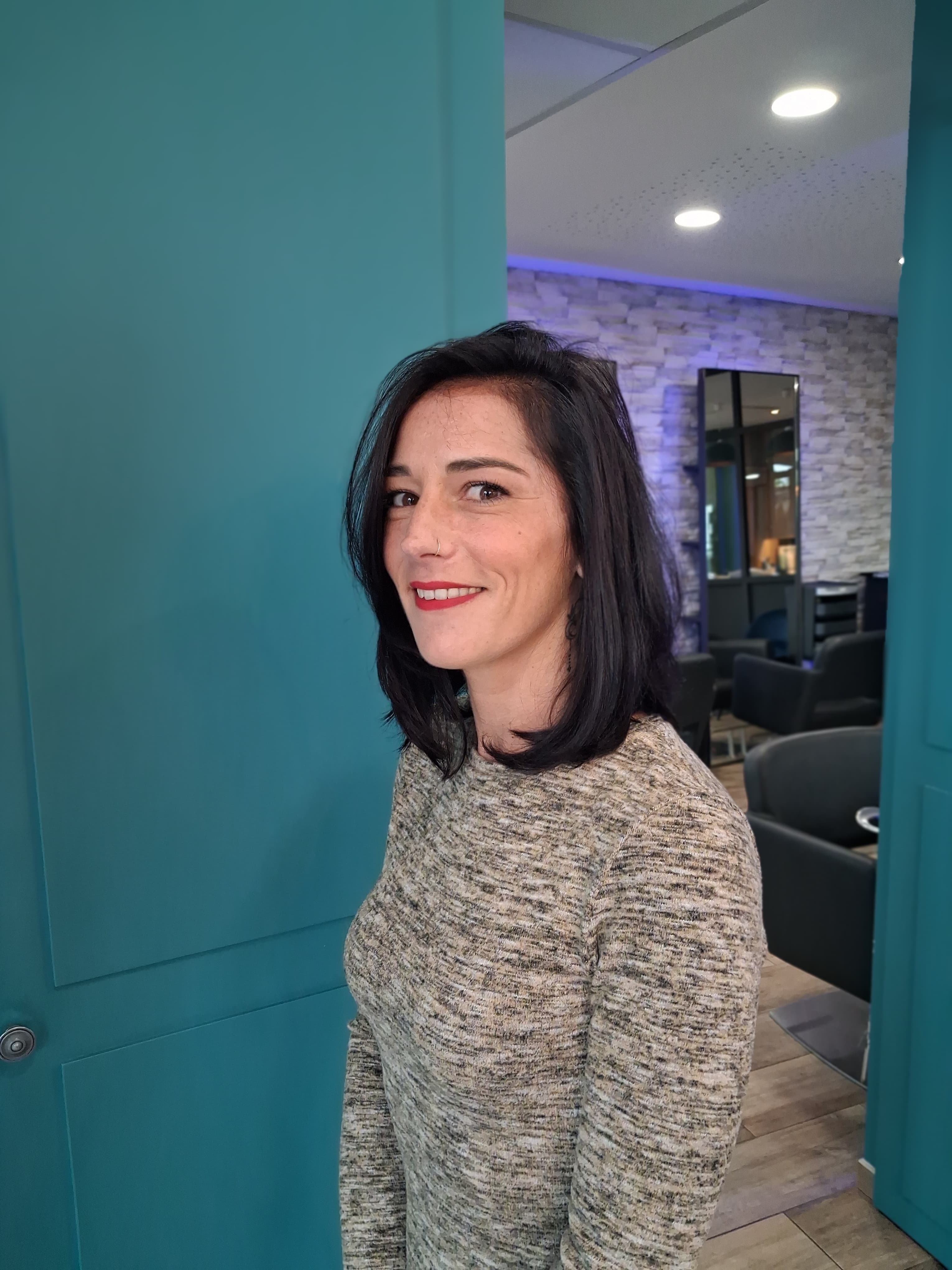 Cheveux longs bouclés avec des mèches blondes vues de dos sur une personne portant un haut rayé blanc et noir.