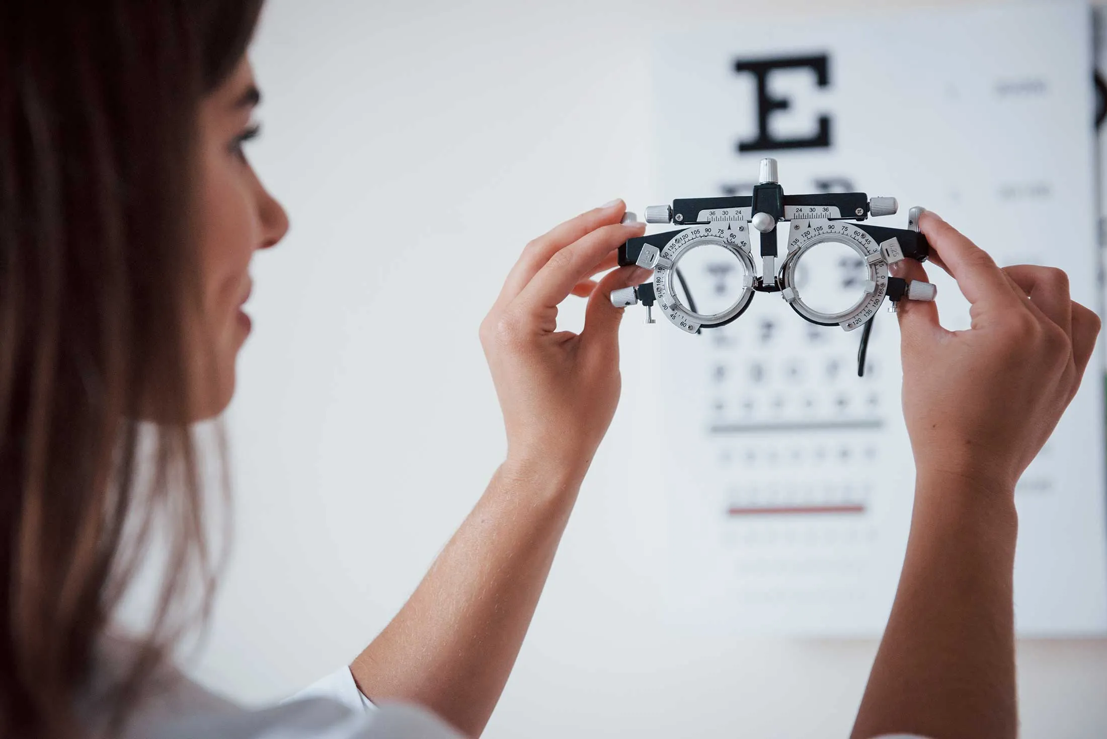 Optometrist adjusting trial frame with eye chart in background