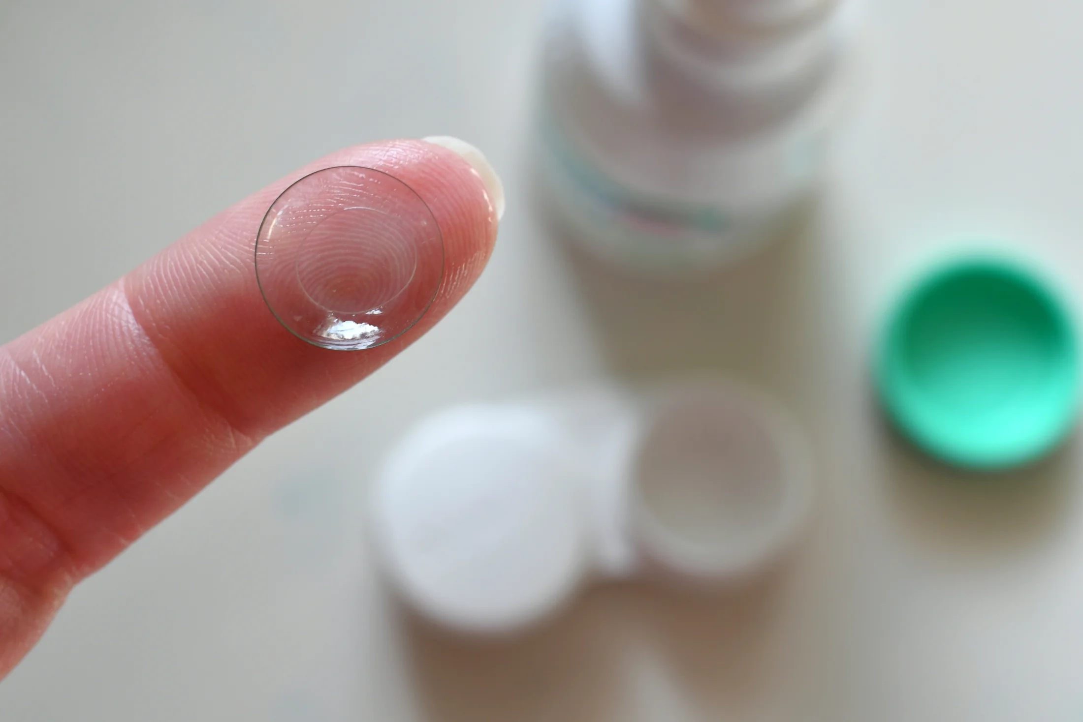 Clear contact lens balanced on fingertip with lens care solution in background
