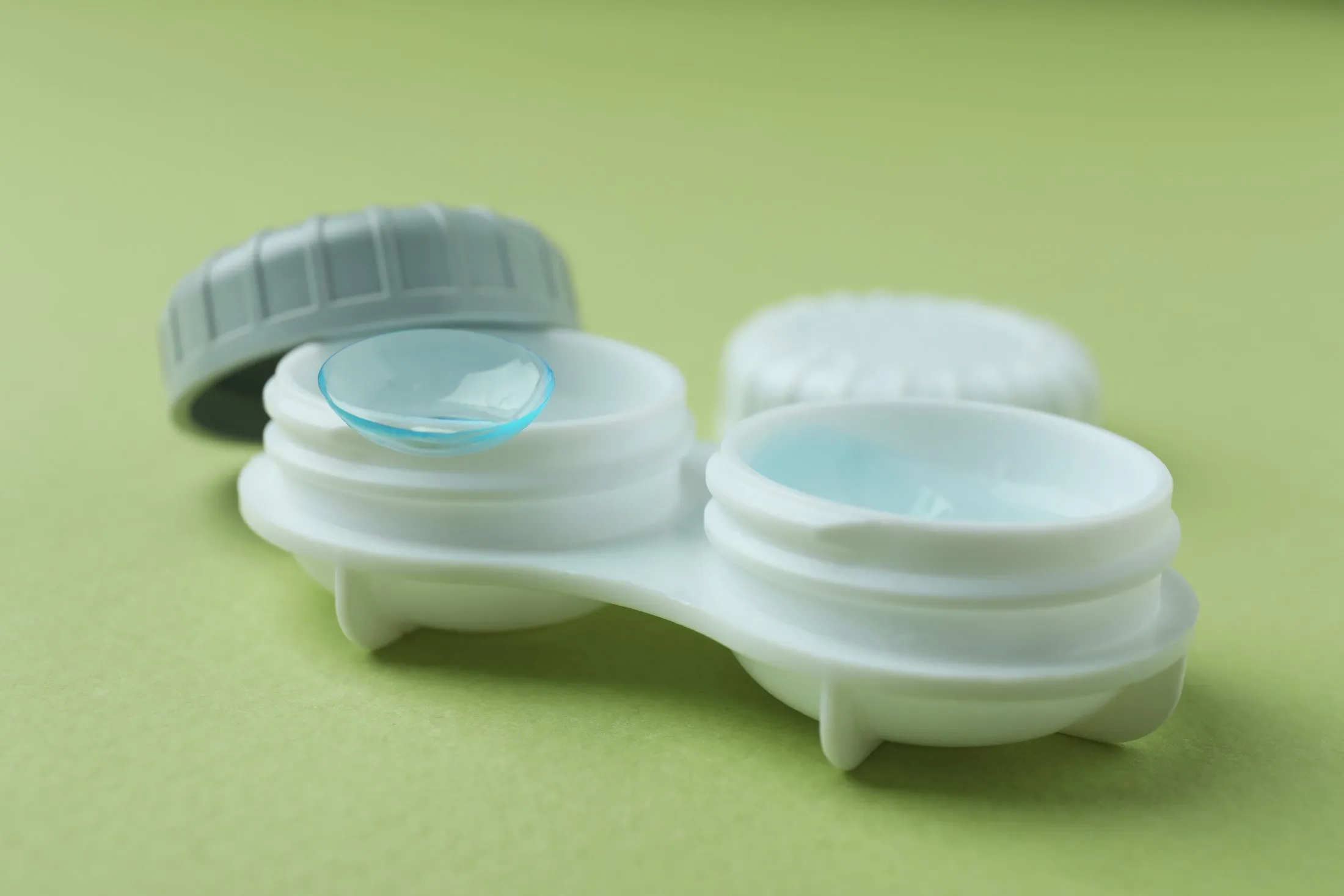 Blue contact lenses in white storage case with gray lid on green background