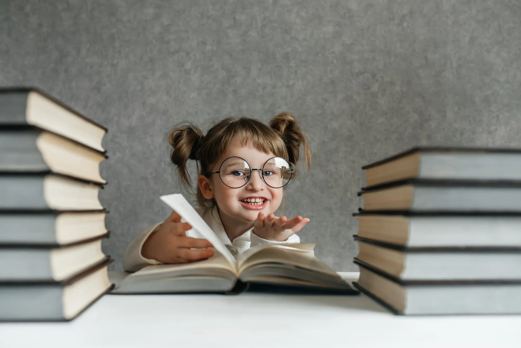 Smiling child with glasses surrounded by books, looking excited about reading