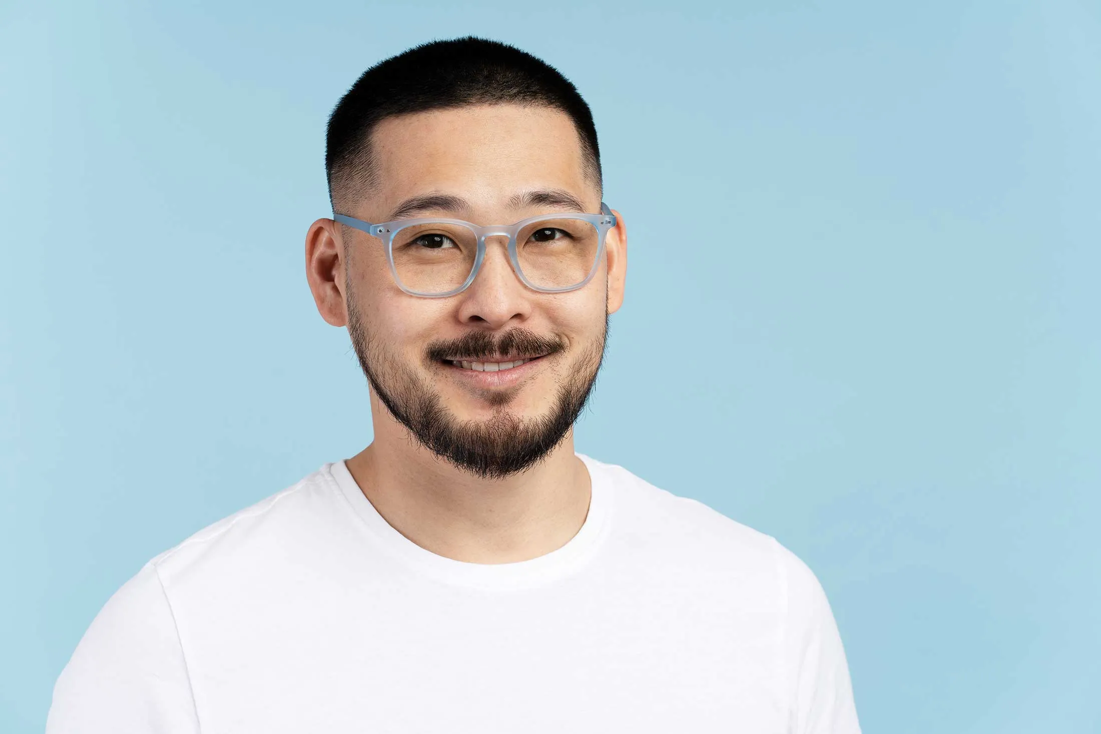 Smiling person with glasses and short hair against blue background