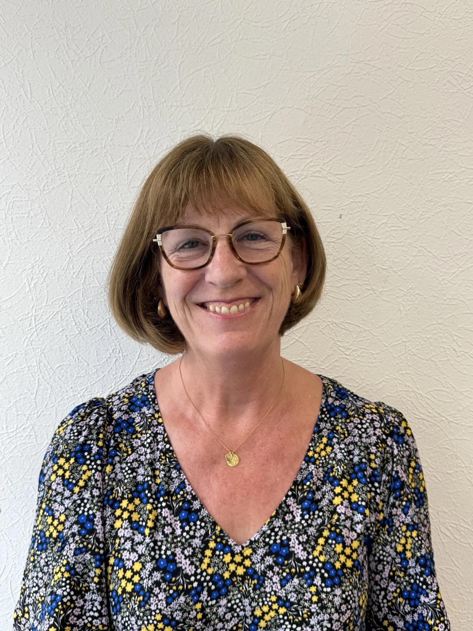 Smiling woman with glasses wearing floral blouse against textured wall