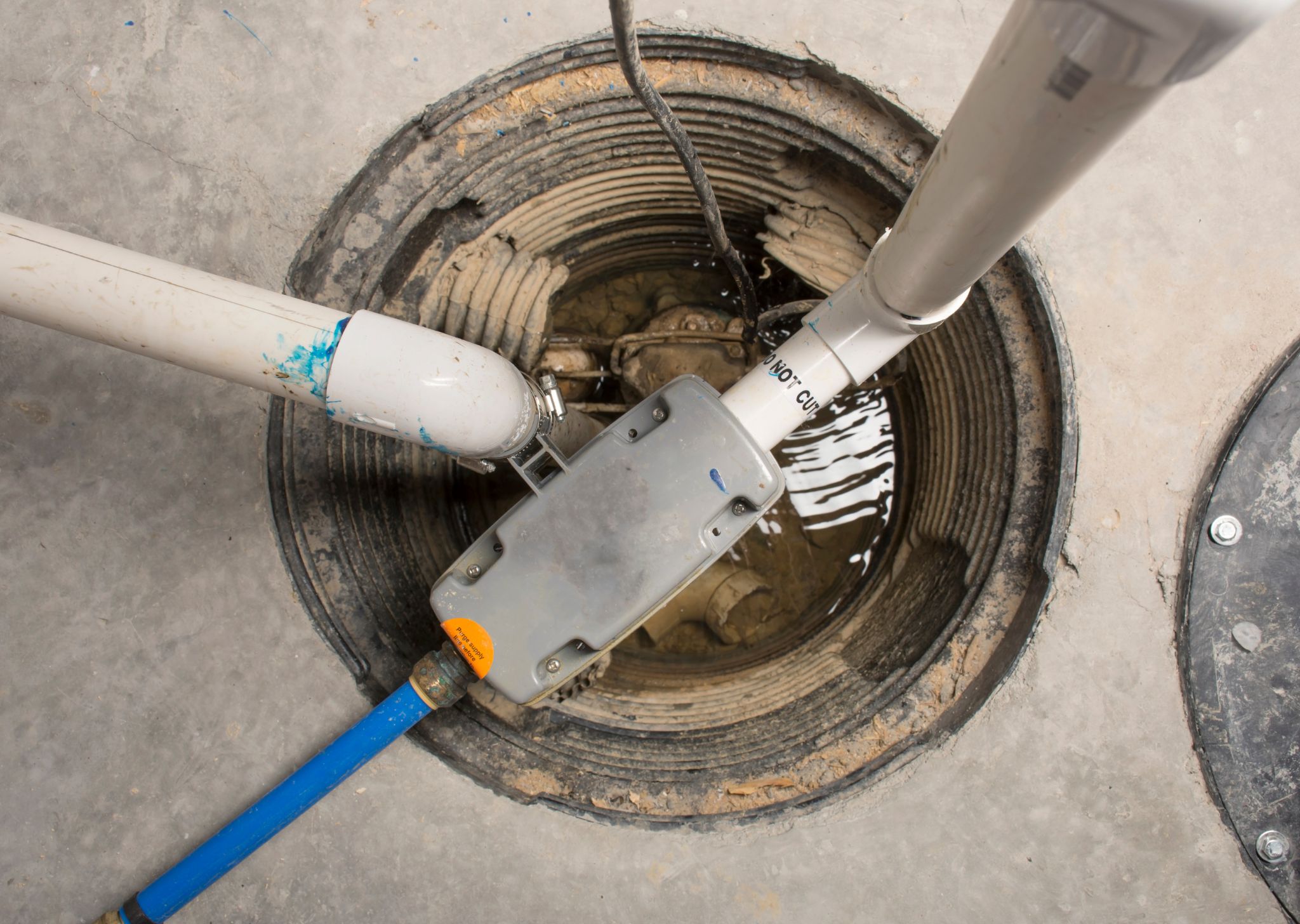 Sump pump system being repaired inside a basement pit to prevent flooding.