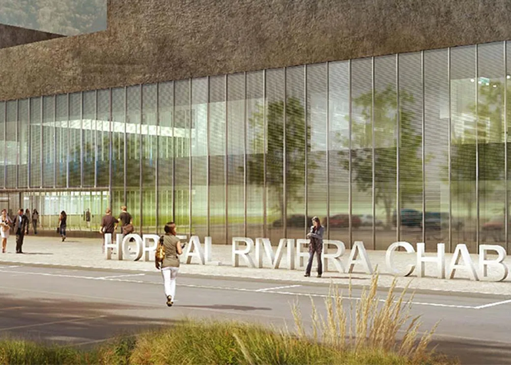 Glass-fronted hospital building with modern architecture and people walking outside.