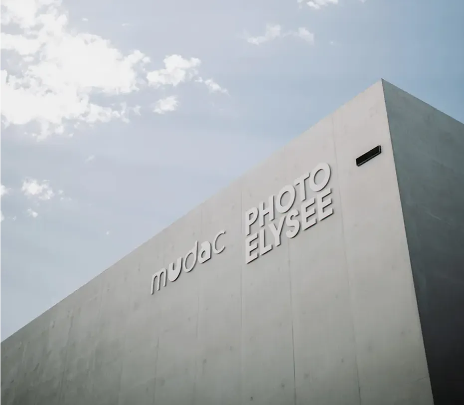 Façade moderne en béton clair du bâtiment mudac Photo Élysée, sous un ciel bleu partiellement nuageux.