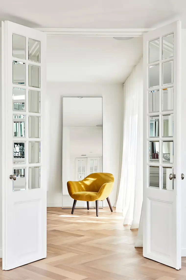 French doors opening onto a yellow armchair and a floor mirror in the Los Angeles studio.