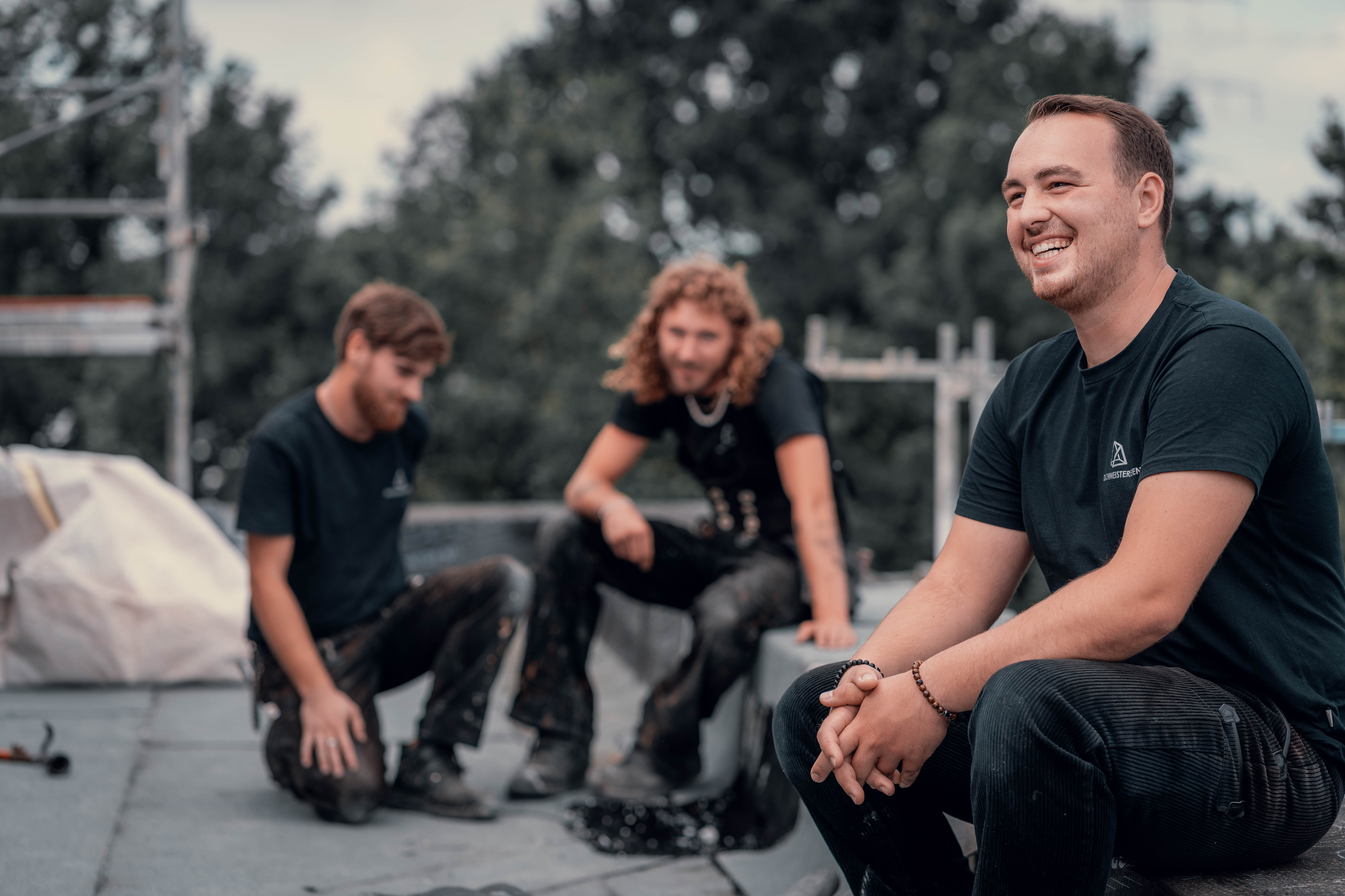 Nino Ellis, Dachdeckermeister aus Osnabrück, sitzt mit seinem Team auf einem Dach – lachend und im Austausch während der Arbeit.