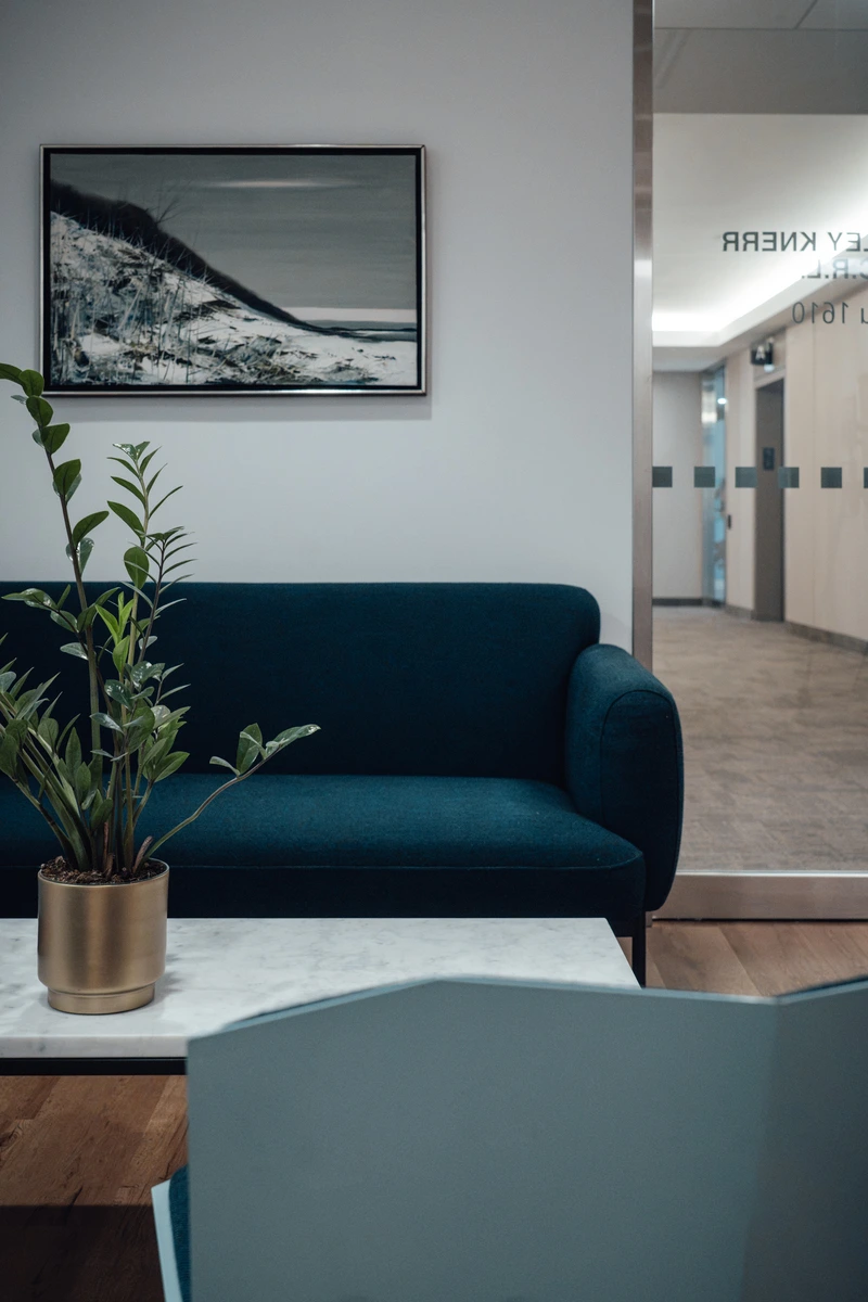 Modern office waiting area with a dark blue sofa, white marble table holding a green potted plant in a gold pot.