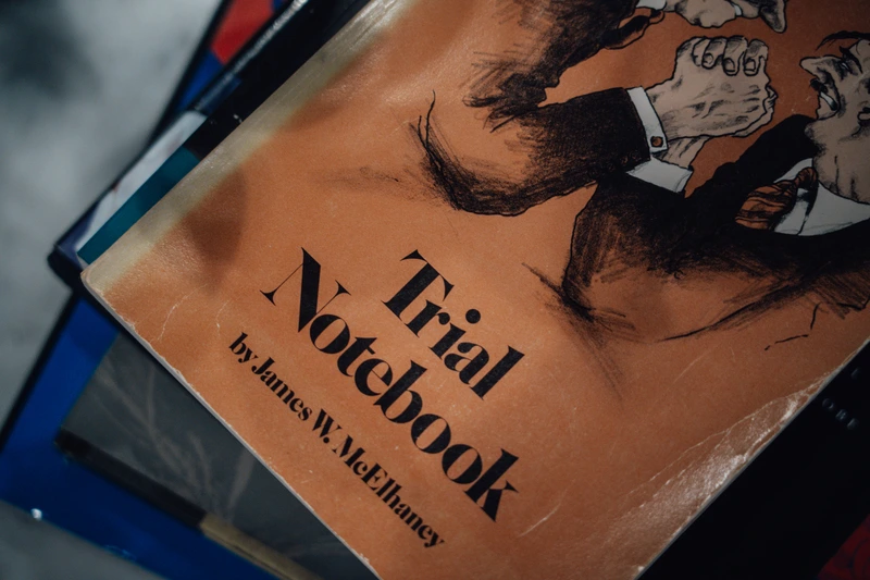 Close-up of an orange book titled 'Trial Notebook' by James W. McElhaney with an illustration of two men arm wrestling on the cover.