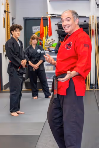 Chief Instructor Sensei Mike smiles at his students while explaining a new technique to their teens karate class.