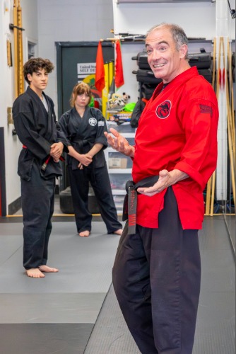 Chief Instructor Sensei Mike smiles at his students while explaining a new technique to their teens karate class.