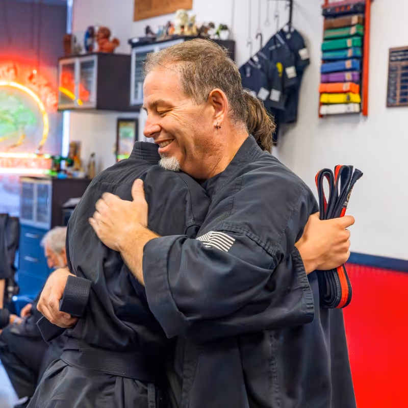 Two karate students exchange hugs after a belt graduation awards ceremony.
