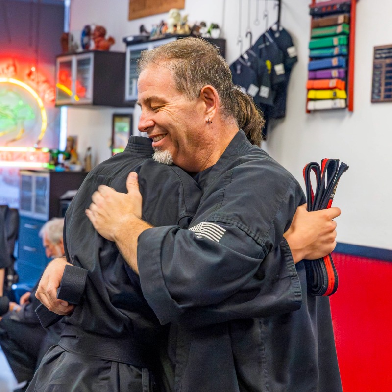 Two karate students exchange hugs after a belt graduation awards ceremony.