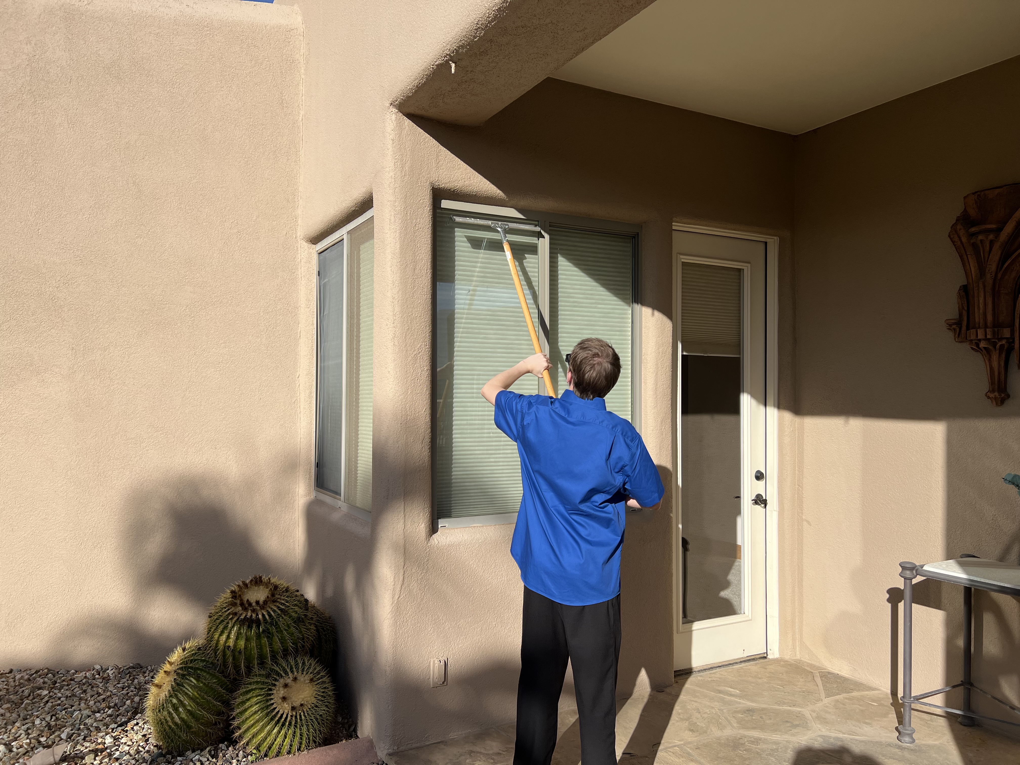 Man in yellow CFTO shirt cleaning the glass door of Falcon Field building in Mesa, Arizona.