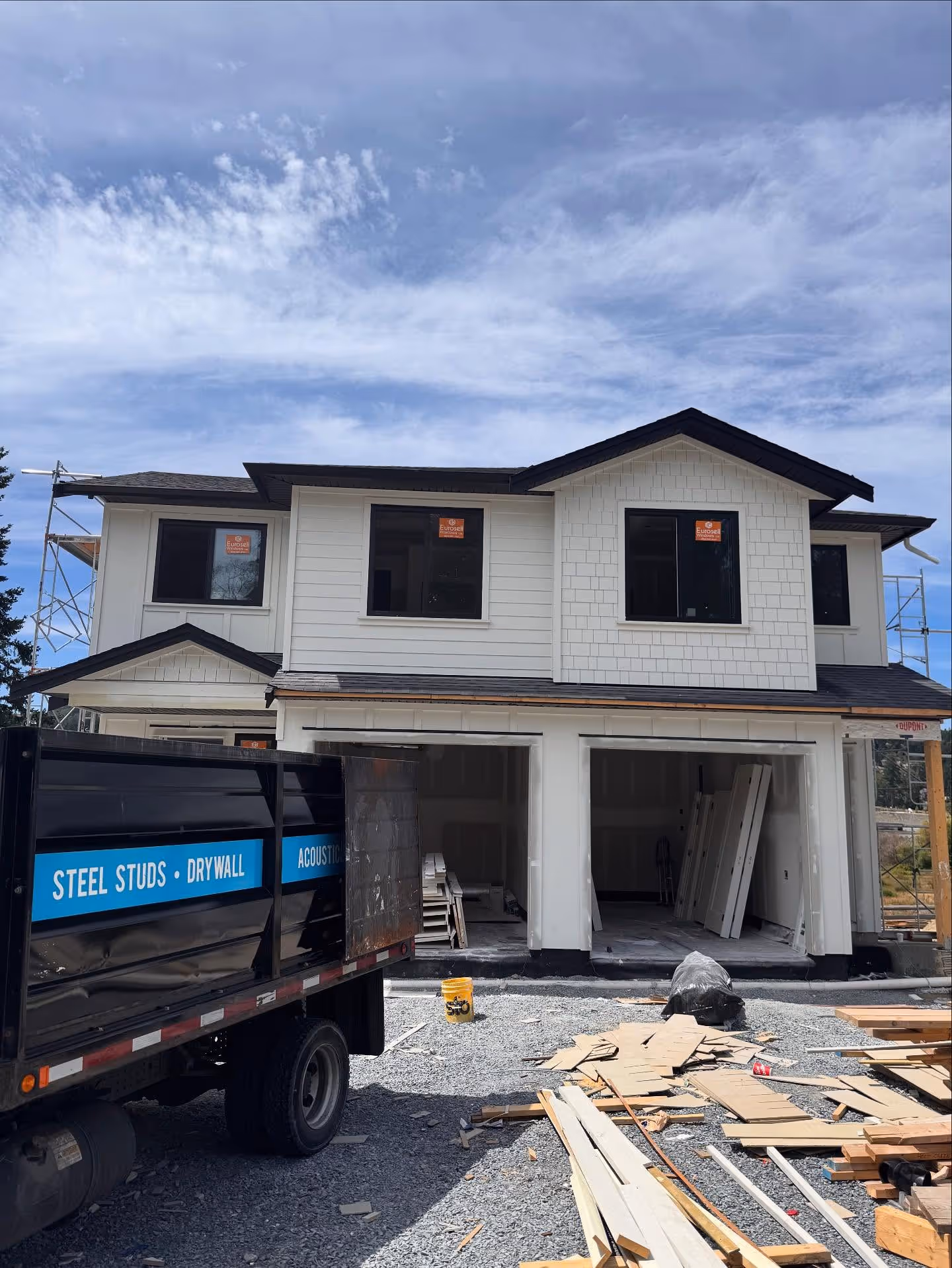 Two-story house under construction with scaffolding, work trucks, and building materials in front.