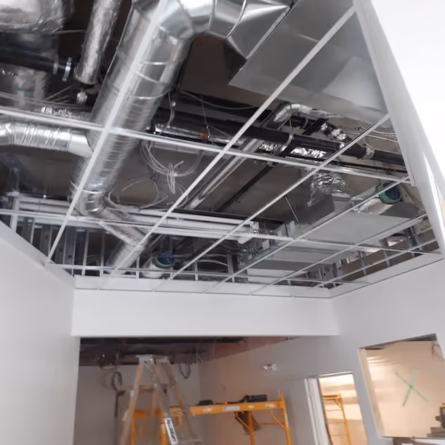 Commercial interior with exposed ceiling showing T-bar grid and ductwork installation.