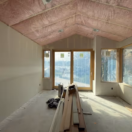 Interior room under construction with pink insulation installed in the ceiling and exposed framing.