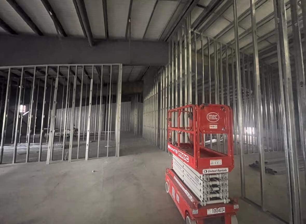 Interior construction site with metal stud framing and a red scissor lift on concrete floor.