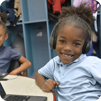 A young girl smiling at the camera while wearing computer headphones 