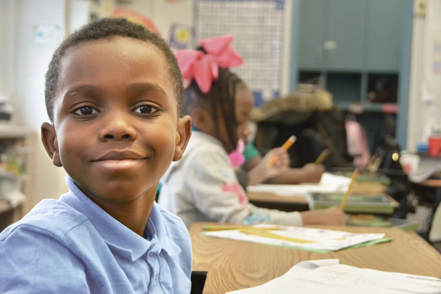 Smiling boy in a classroom with students working in the background.