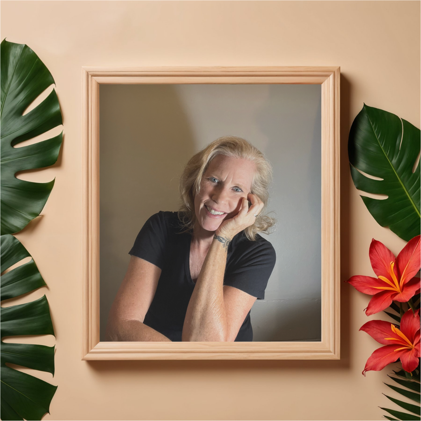 portrait picture of Laura Cavanaugh in a brown frame hanging on a beige wall with green plant leaves surrounding the picture, the woman in the picture is smiling and wearing a black v-neck t-shirt.